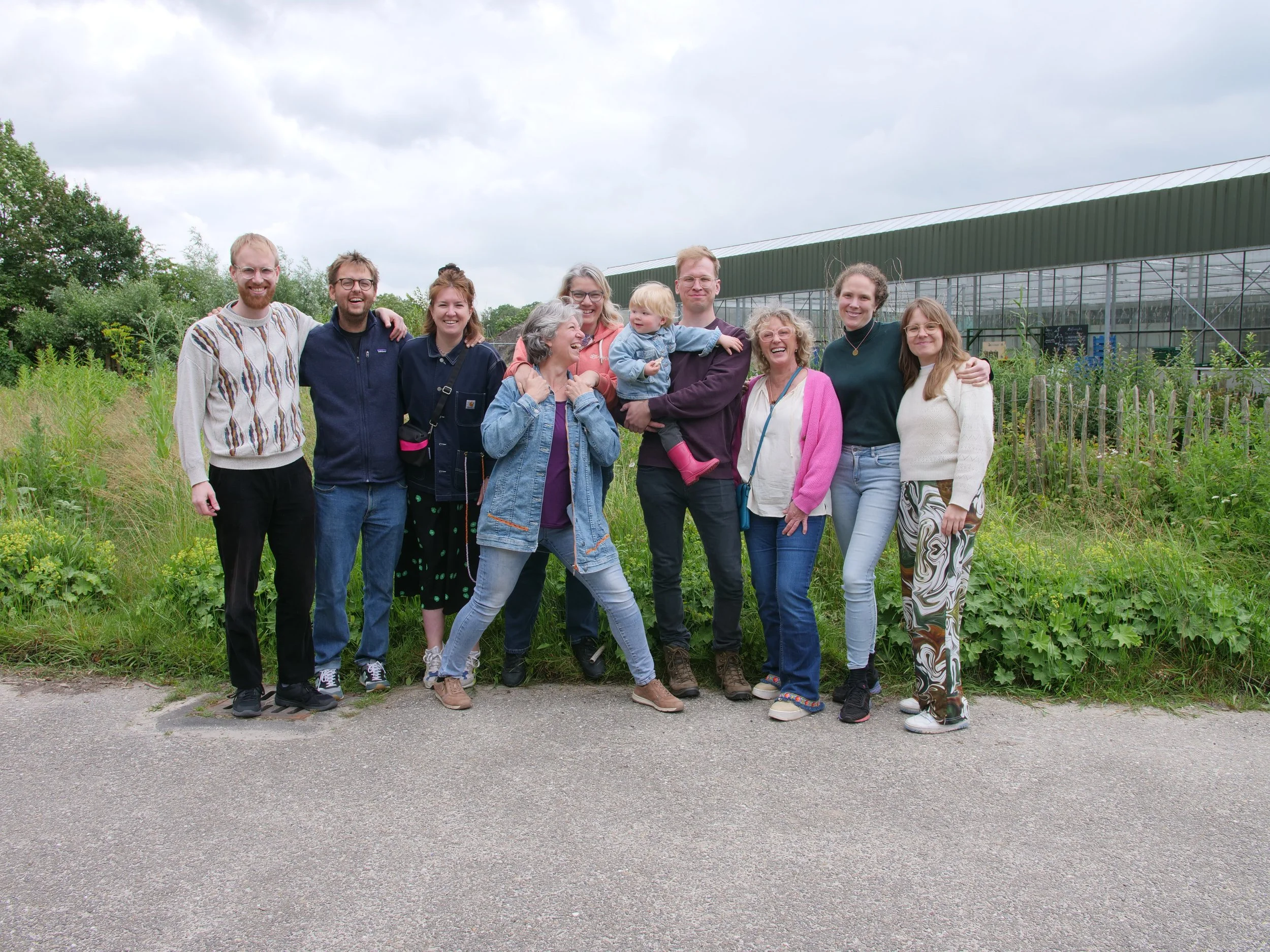 Groep mensen die samen lachen en poseren buiten, met een groene kas op de achtergrond.