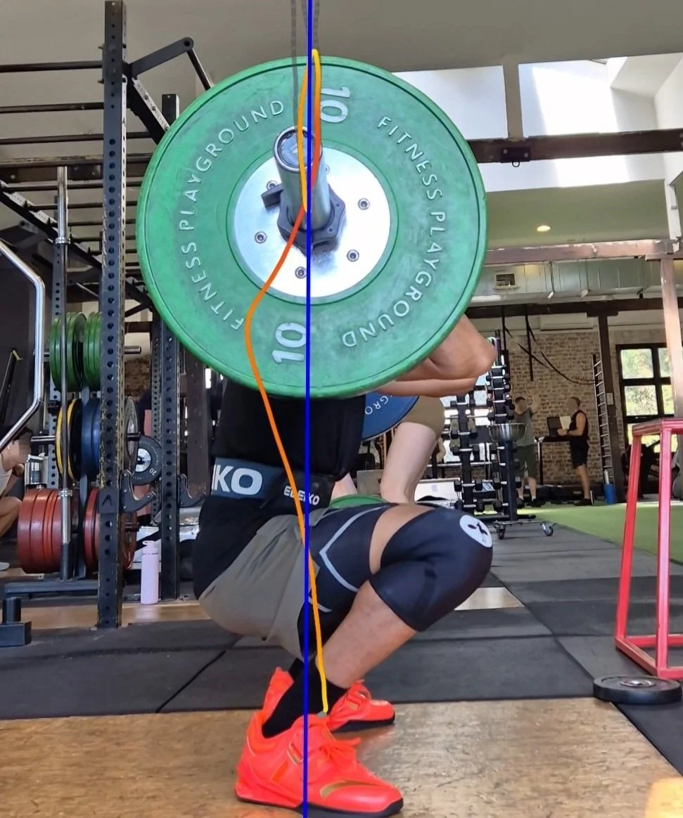 Person performing barbell squat with green weight plates in a gym