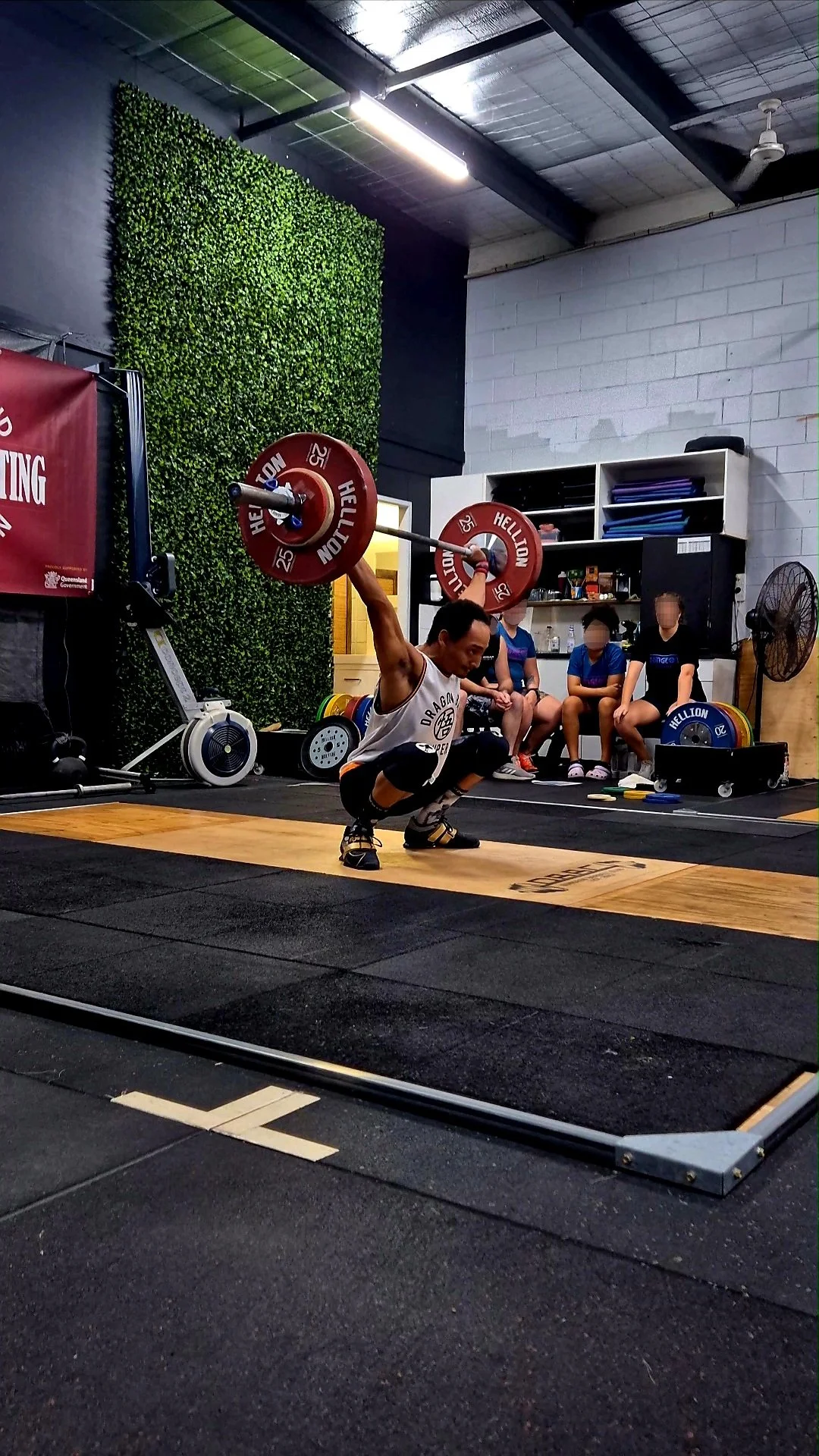 Man performing a snatch lift in a gym, surrounded by spectators.