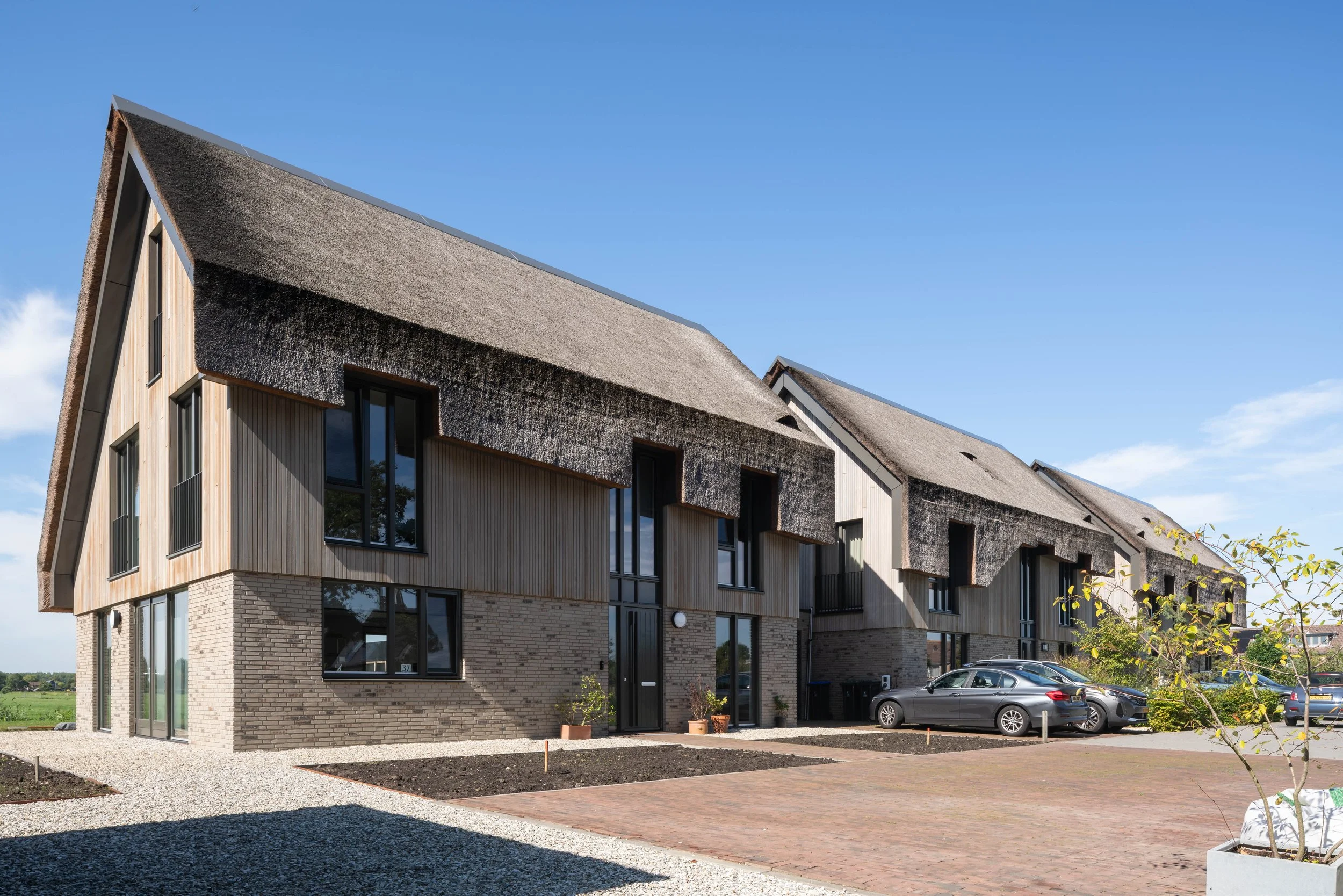 Straataanzicht van een nieuwbouwwoning met een rietgedekt dak, houten gevelbekleding en grote raampartijen in Nederhorst den Berg als nieuwbouw woningbouw ontwerp.