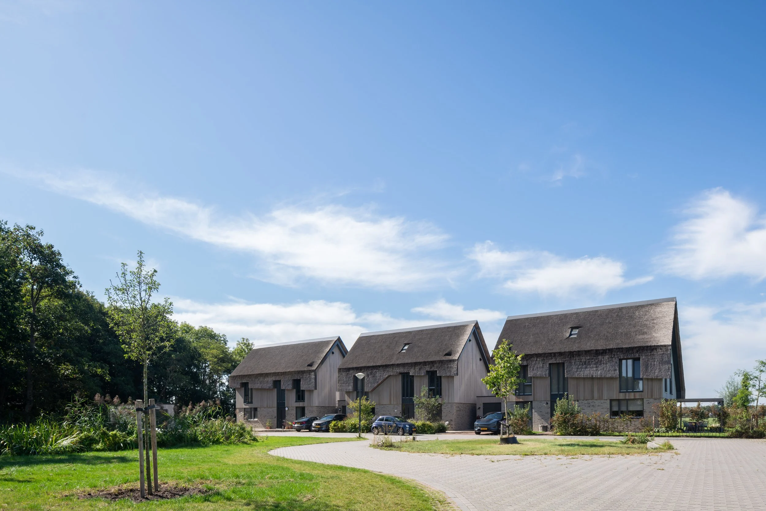 Drie nieuwbouwwoningen met rieten daken en houten gevels in een groene omgeving in Nederhorst den Berg als voorbeeld van landelijke nieuwbouw woningbouw architectuur.