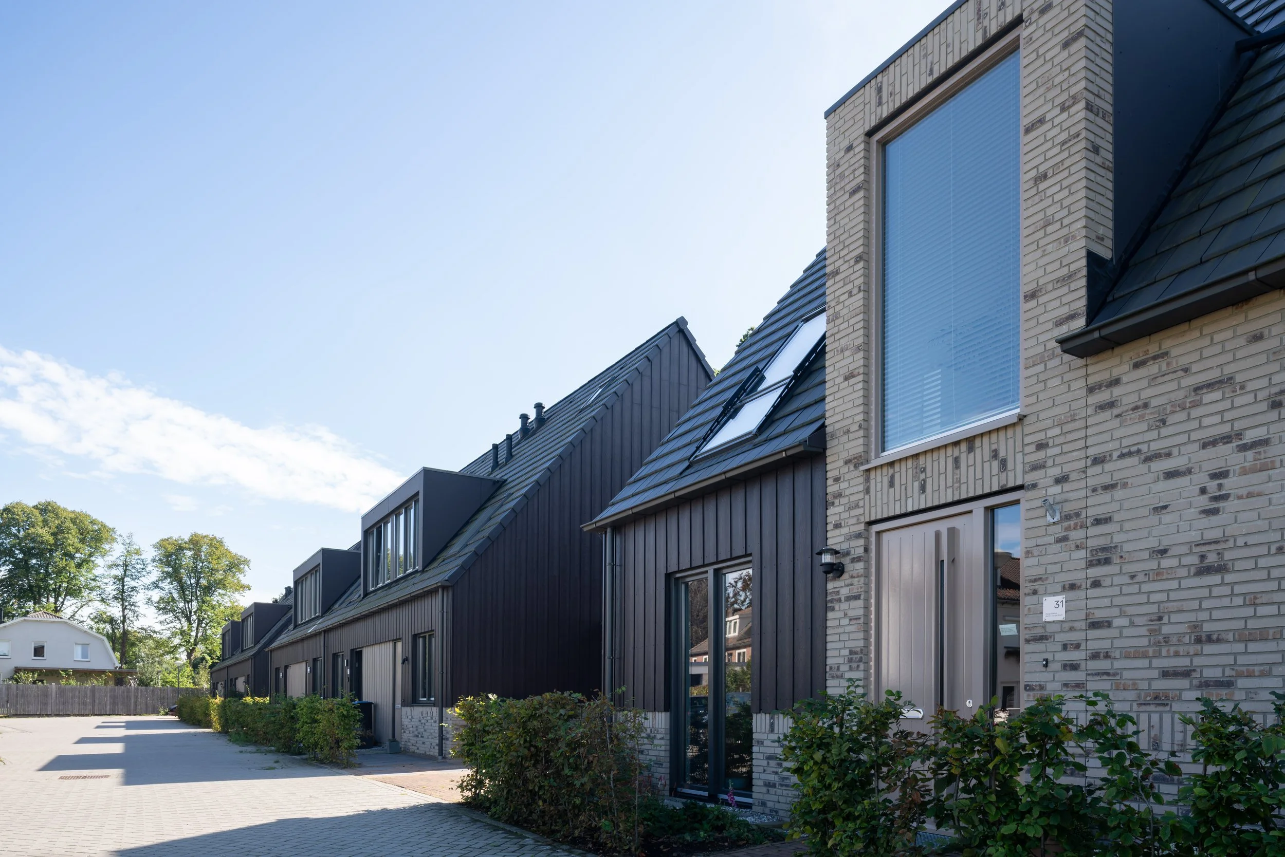 Gevelaanzicht van een nieuwbouwvilla met een hoge spitse gevel in gemêleerde lichte baksteen met grote raampartijen en een balkon in Nederhorst den Berg.