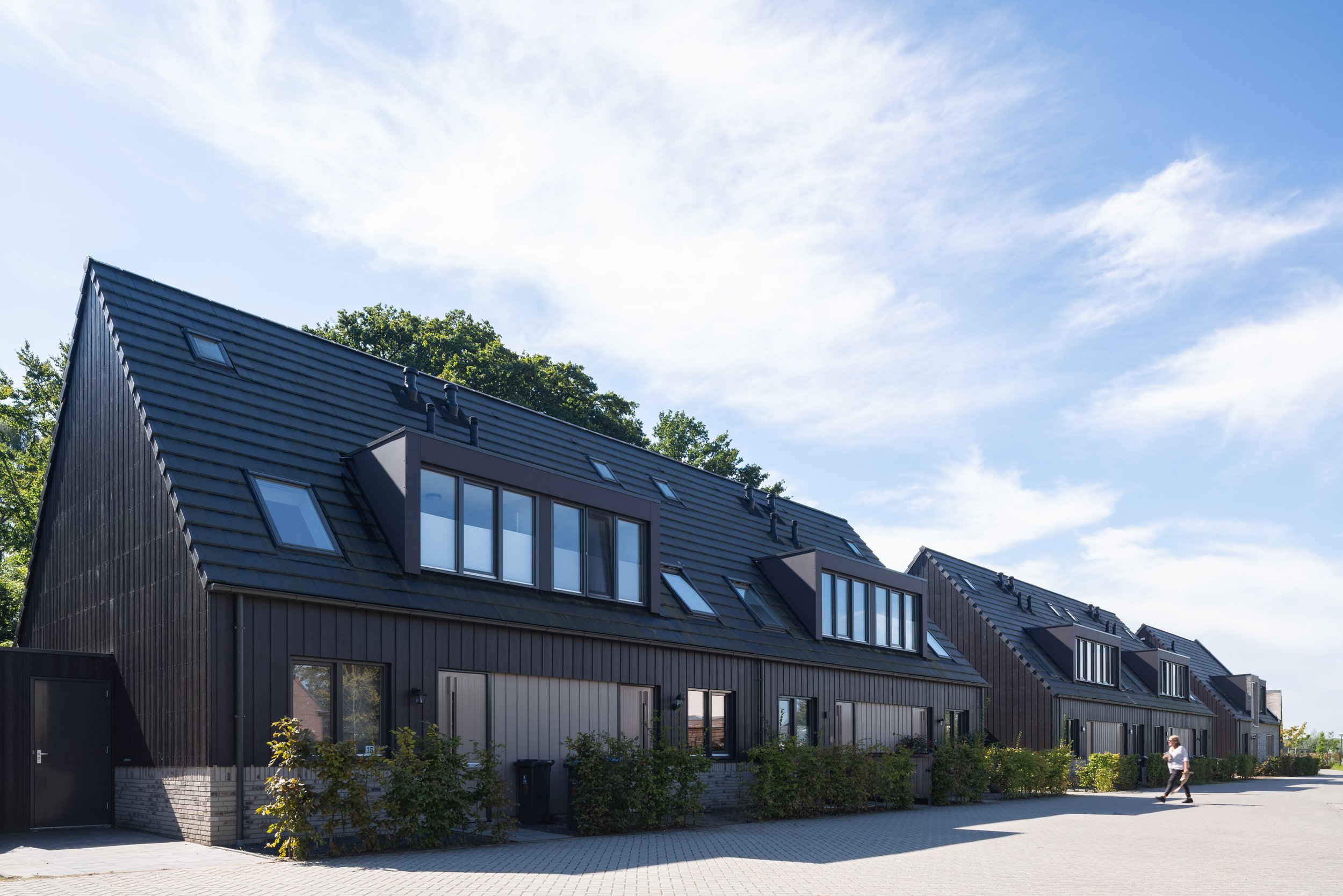 Een rij nieuwbouwwoningen in Nederhorst den Berg met donkere verticale houten gevelbekleding, een leien dak met dakkapellen en een lichte bakstenen plint als woningbouw architectuur.