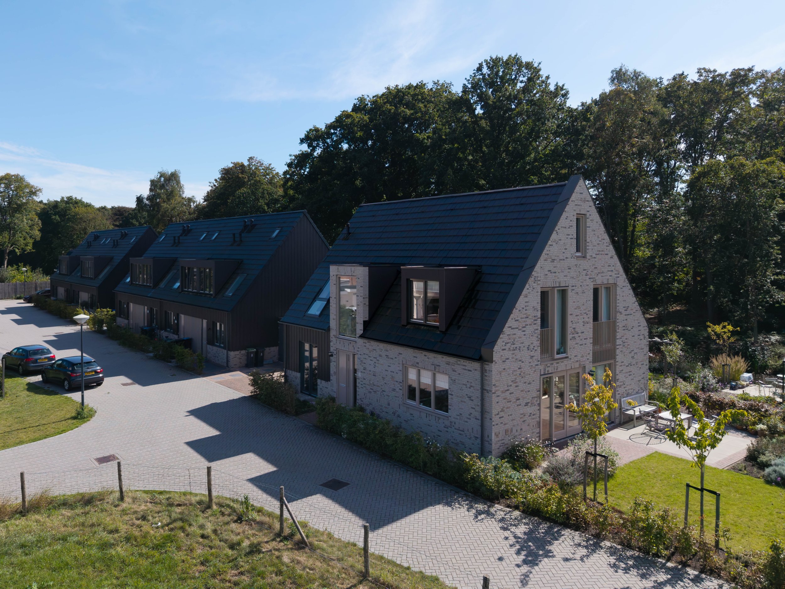 Een droneaanzicht van nieuwbouwwoningen met donkere leien daken en lichte bakstenen gevels met een tuin en bomen in Nederhorst den Berg als nieuwbouw woningbouw.