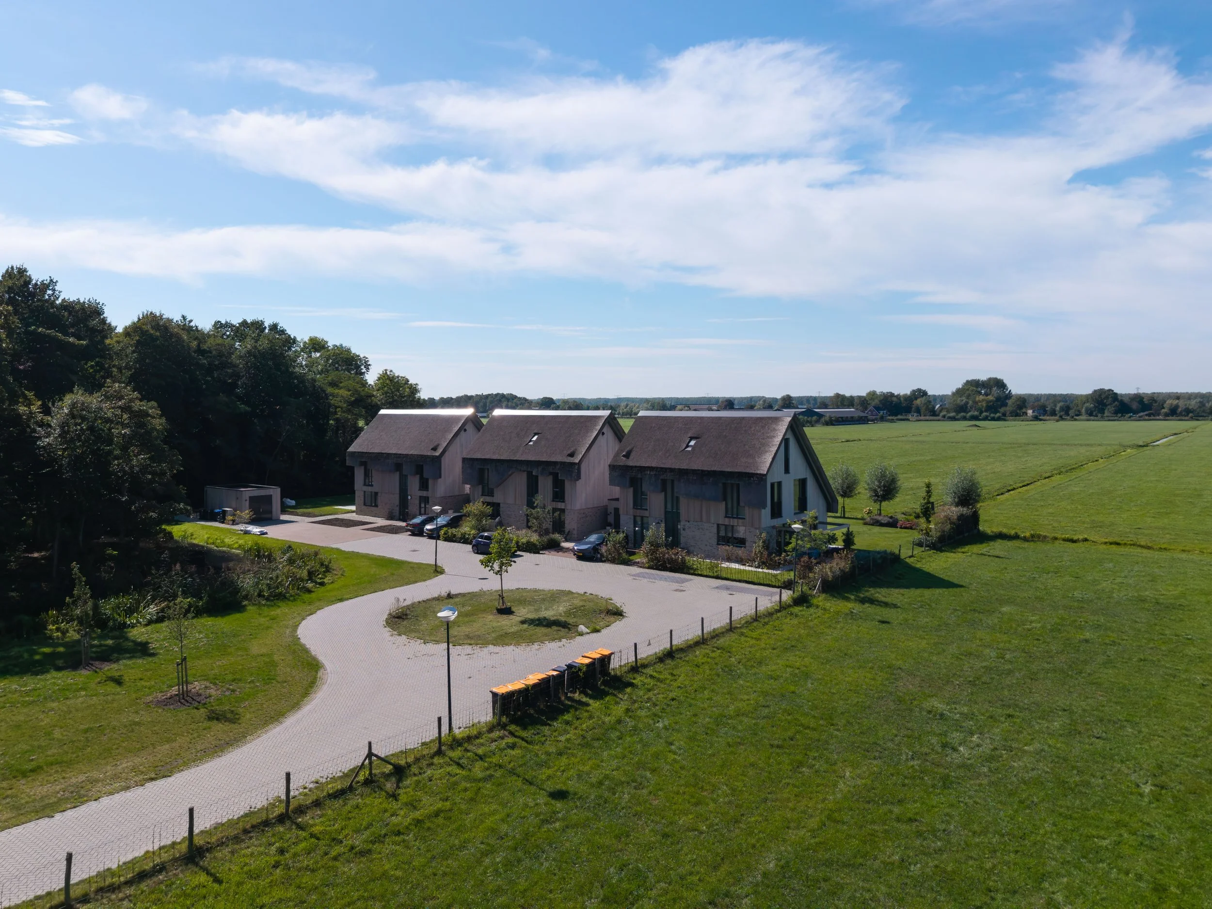 Een droneaanzicht van het nieuwbouwproject in Nederhorst den Berg met rieten daken en houten gevels in een groene landelijke omgeving als woningbouw projectontwikkeling.