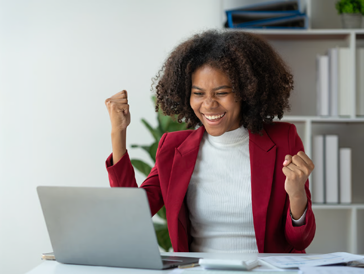 A happy woman celebrating a productivity win while looking at her laptop.