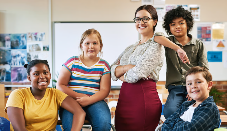 A smiling school teacher posing with her diverse students in a classroom.