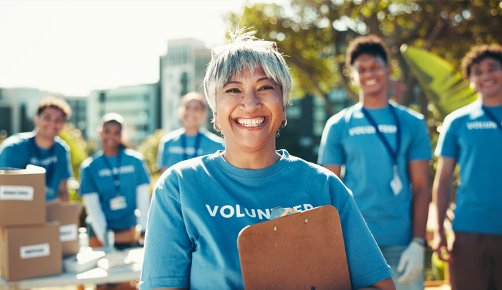 A happy woman with a clipboard leading a group of community volunteers.