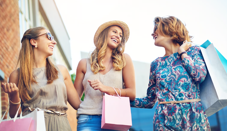 Three happy friends carrying shopping bags down a retail fashion street.