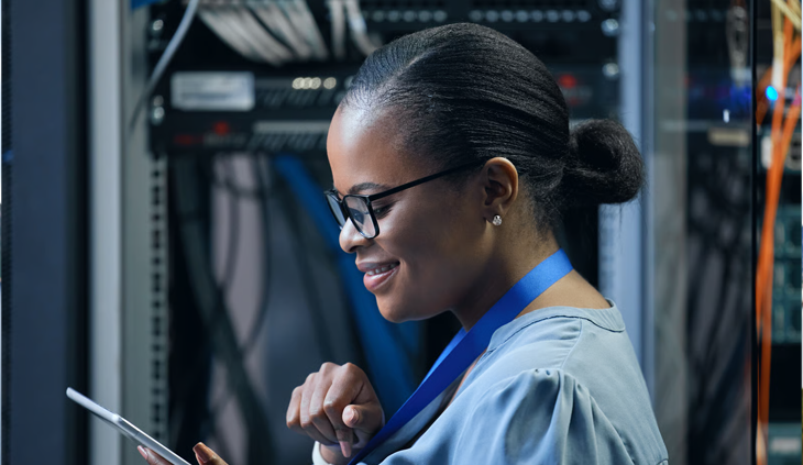 A smiling IT specialist using a digital tablet in a secure server room.