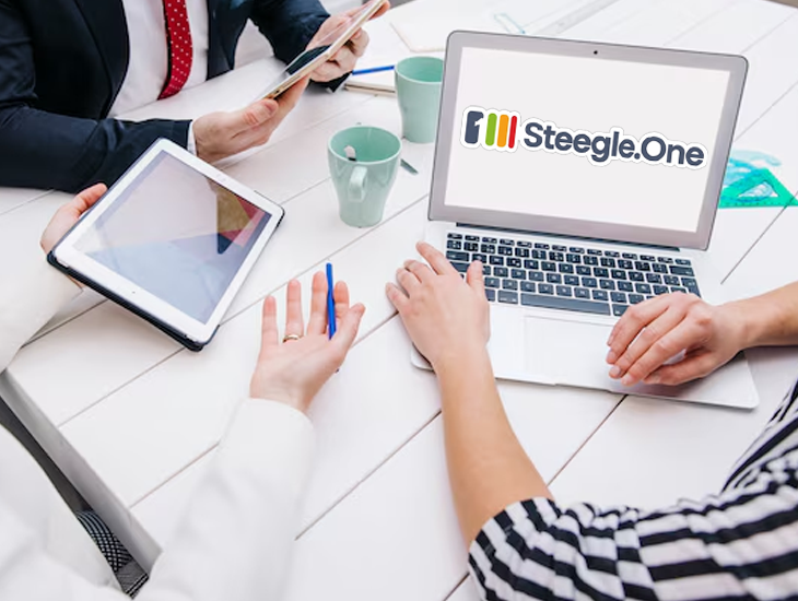 Steegle.One logo displayed on a laptop screen with people gathered around it.