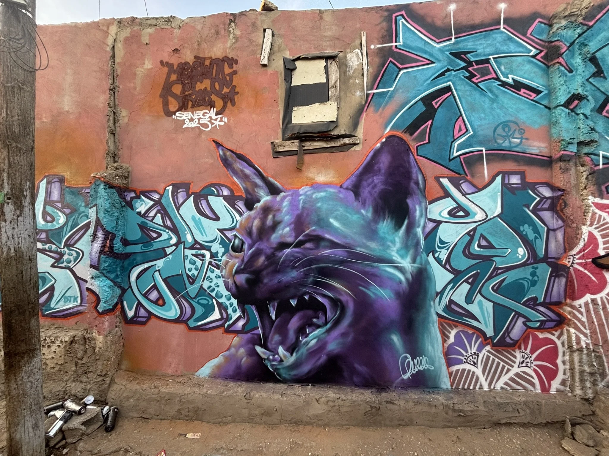 Colorful graffiti mural of a snarling cat with purple, blue, and black fur, surrounded by intricate blue and teal graffiti lettering and designs on an urban wall.