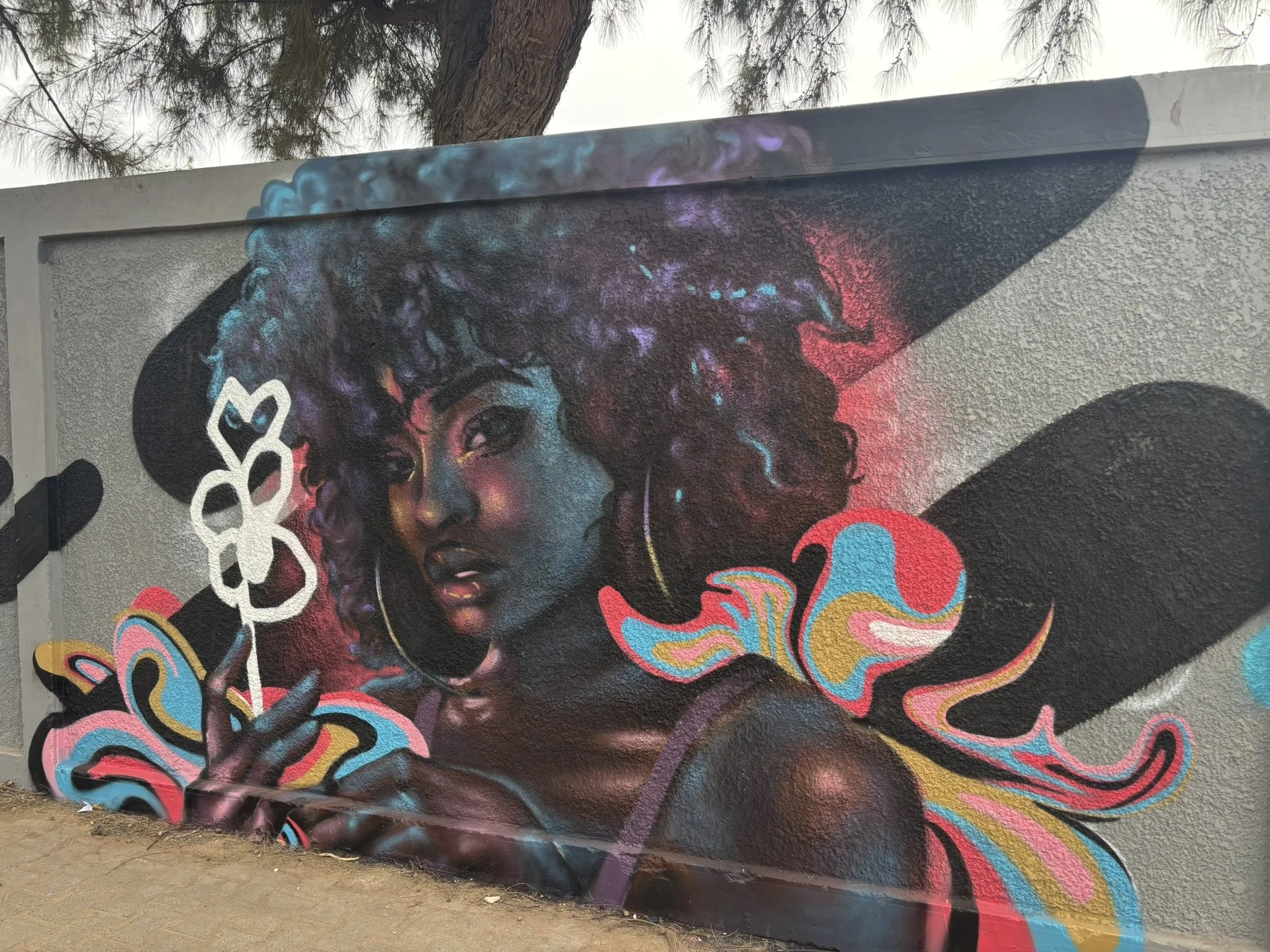 Colorful mural of a woman with curly hair holding a white flower; vibrant, swirling patterns surround her.