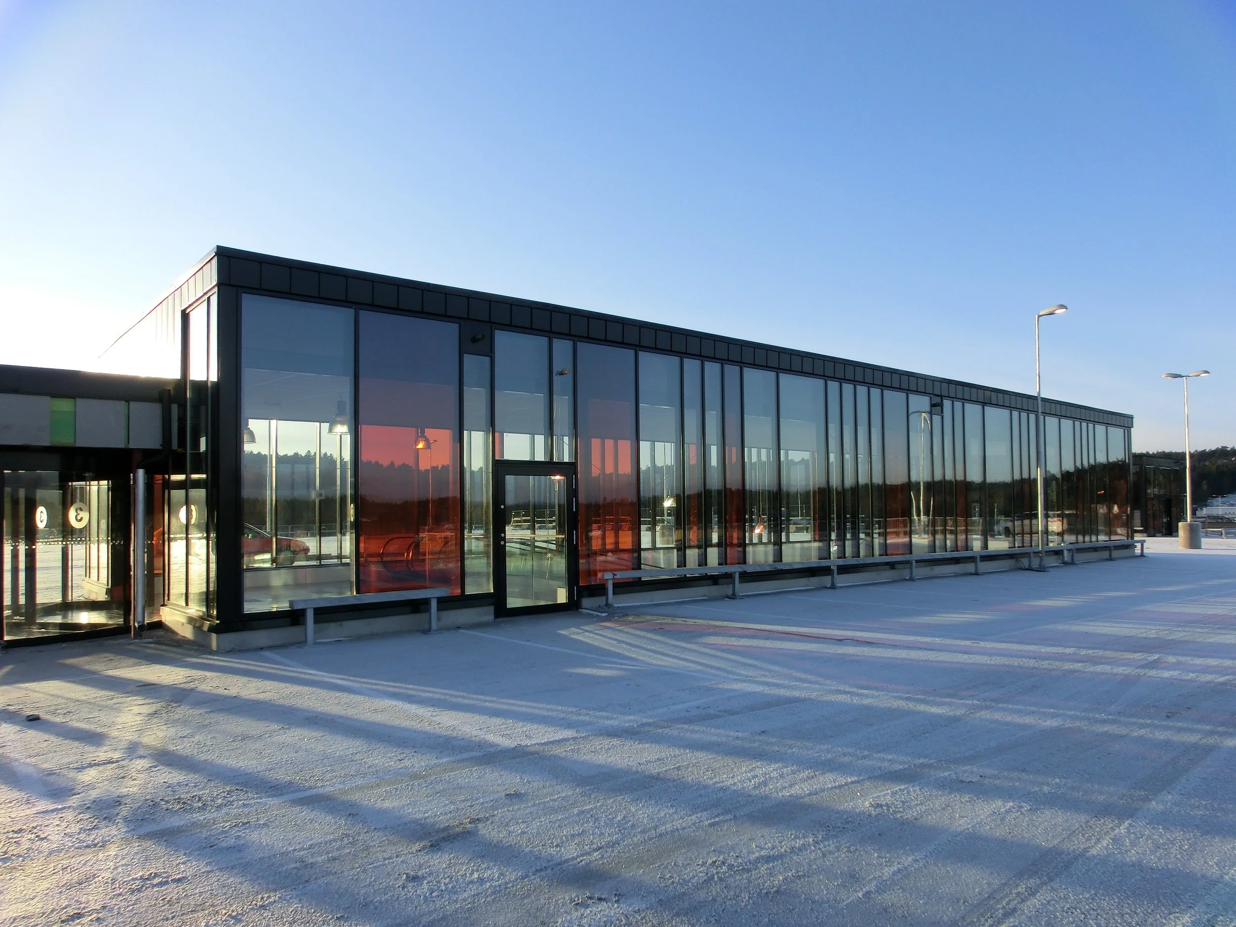 Modern en-våningsbyggnad med stora glasfönster och snöig utomhusmiljö, troligen en buss- eller tågstation.
