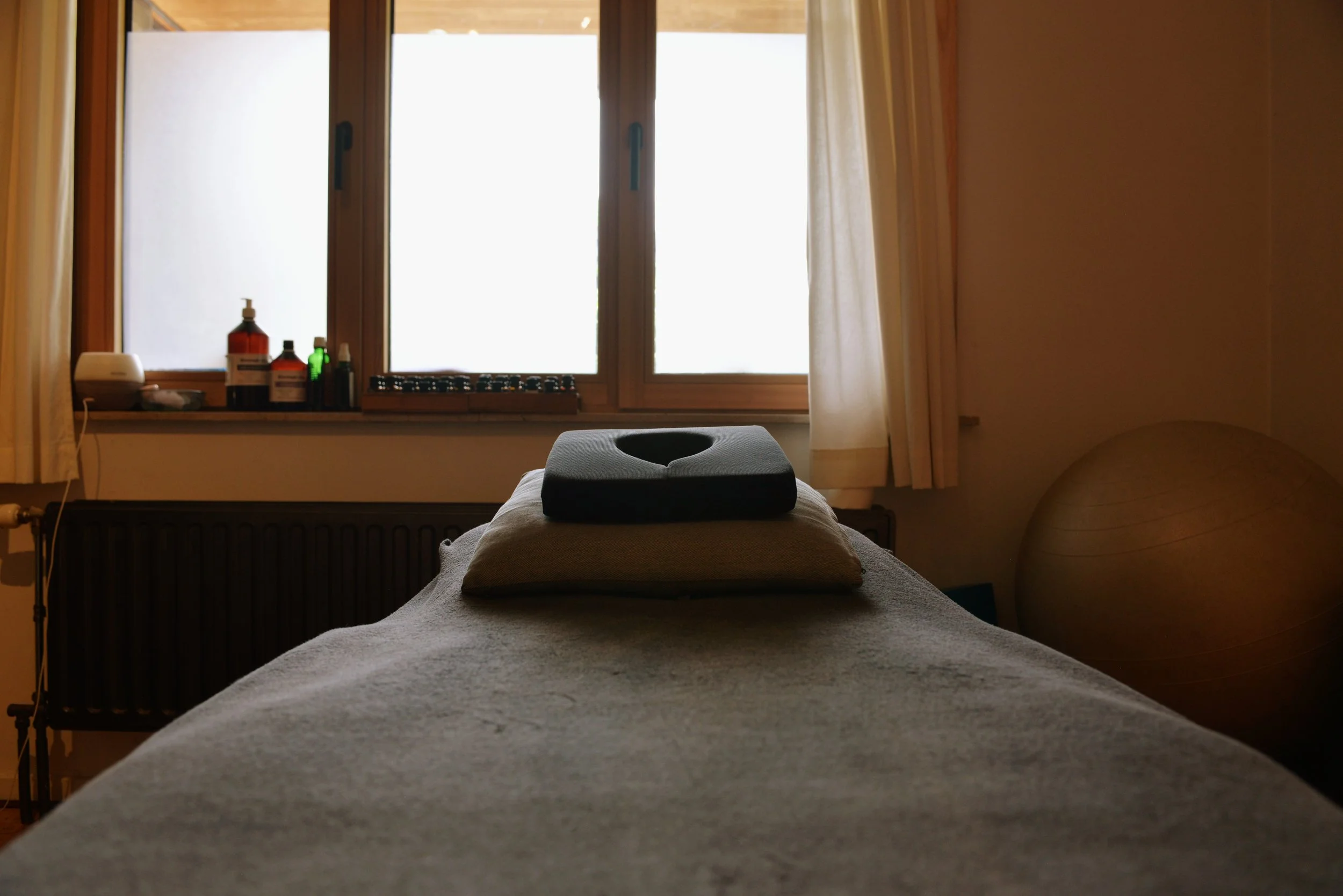 A massage table with towels in front of a window with curtains, in a softly lit room.