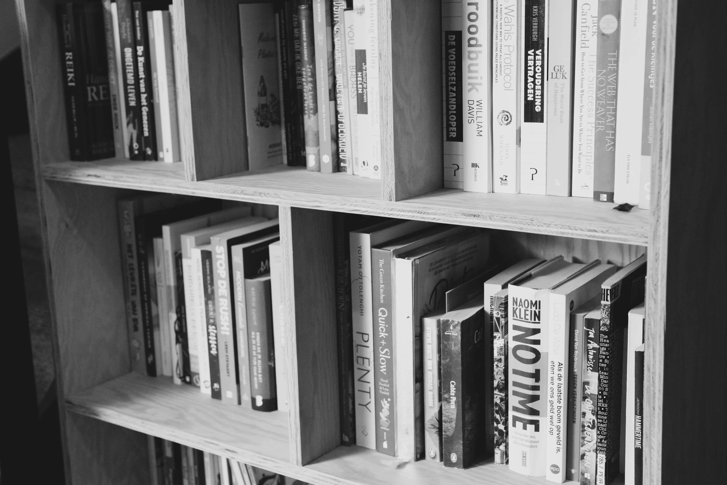 A wooden bookshelf filled with various books in black and white.