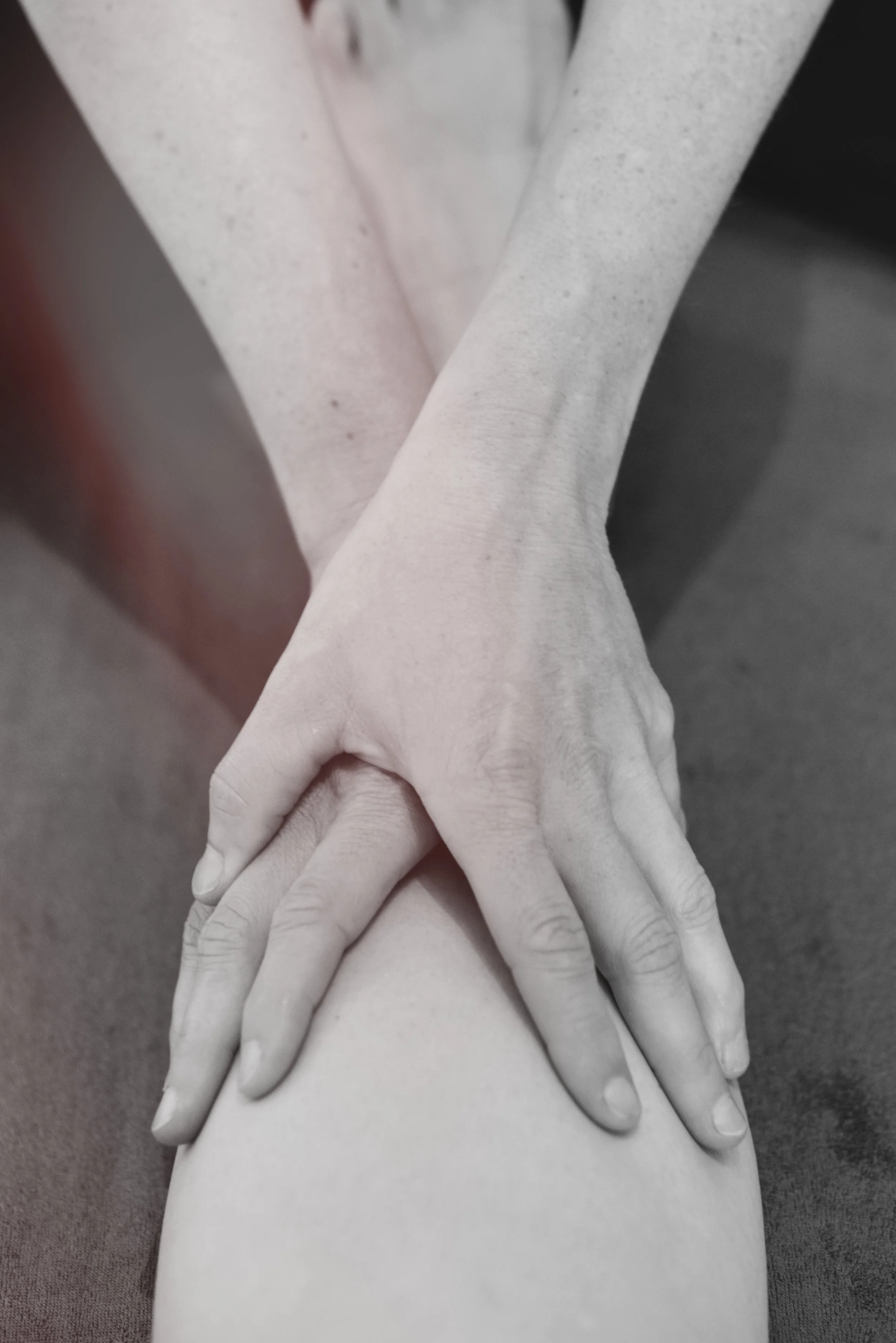 Close-up of two hands, one placed over the knee of a person, with the background blurred.