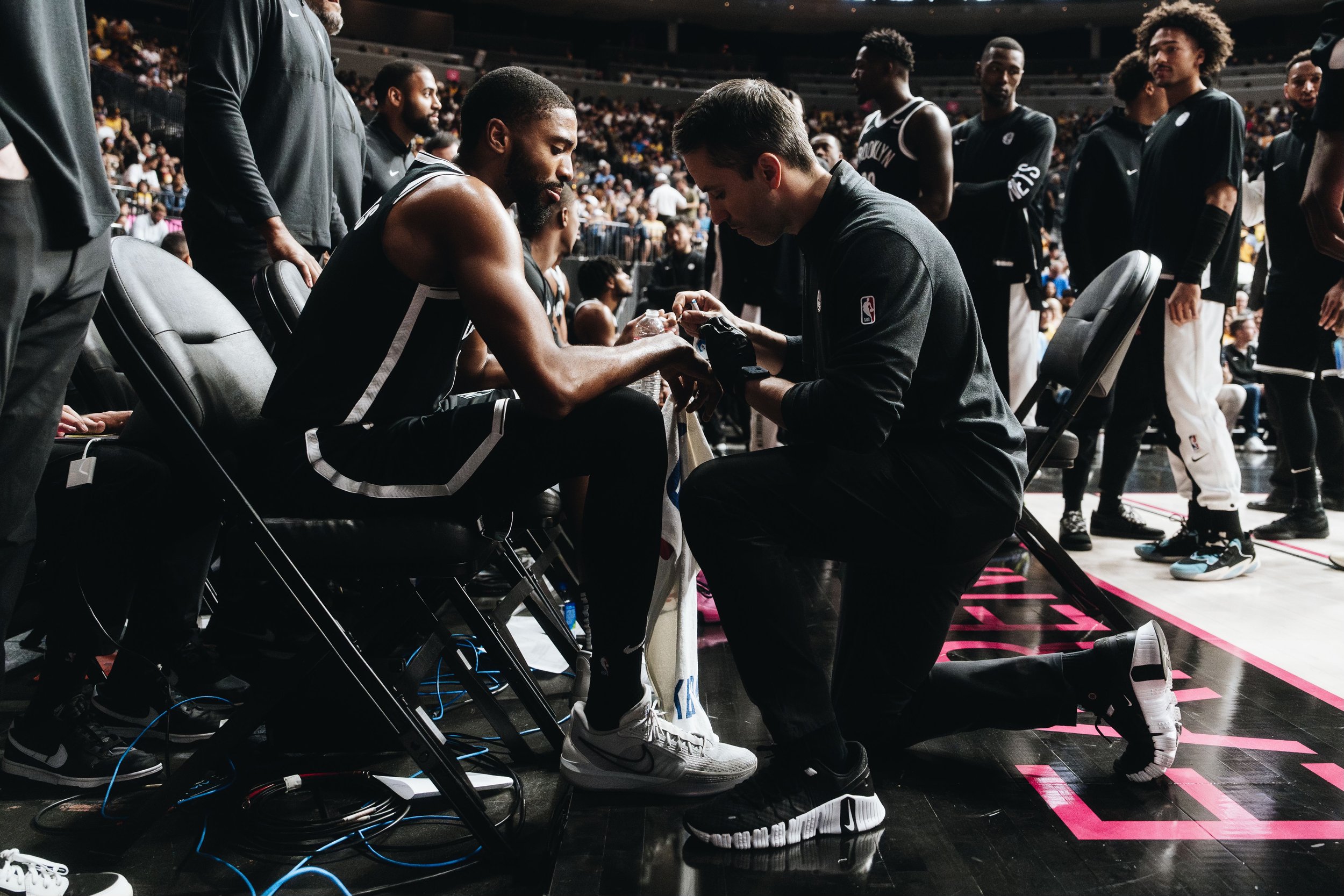 A basketball player receiving medical attention on the sideline during a game, with teammates standing around in the background.