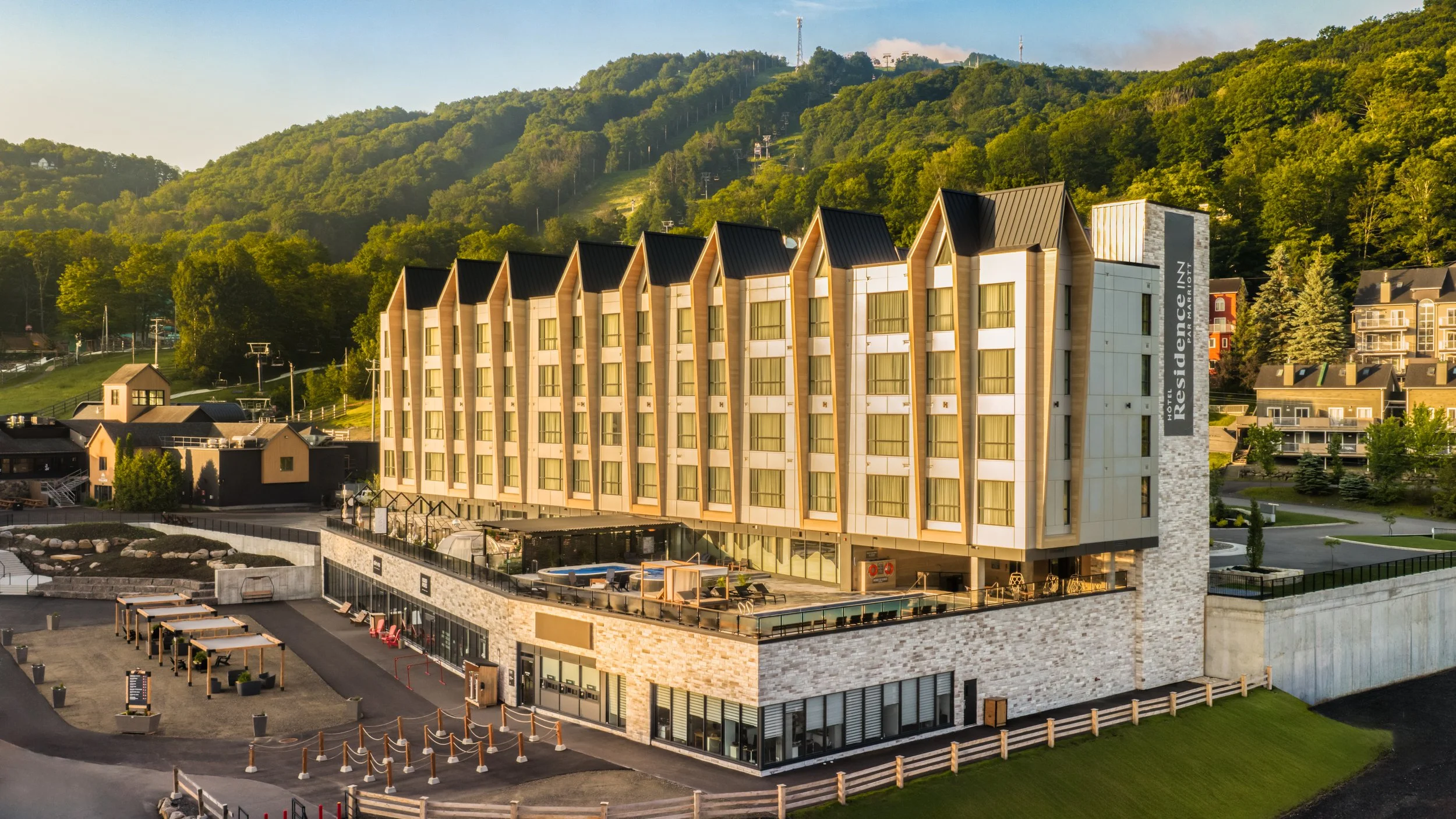 A modern hotel building with a distinctive design, located at the base of a green hillside, with a sign reading "Residences Inn by Marriott" on the side of the building.