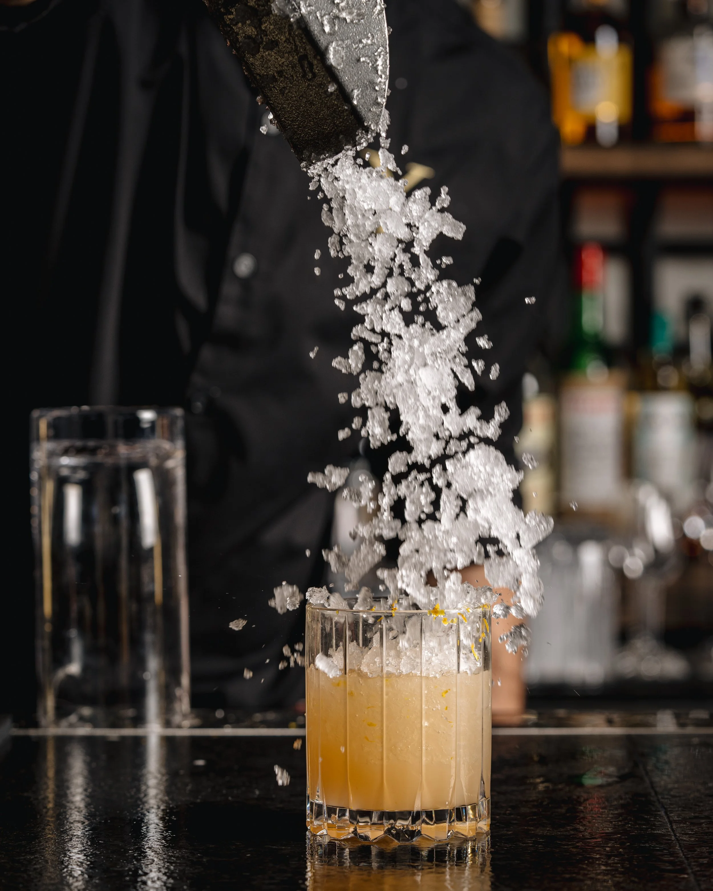 A close-up of a glass of beer with ice falling into it, causing a splash.