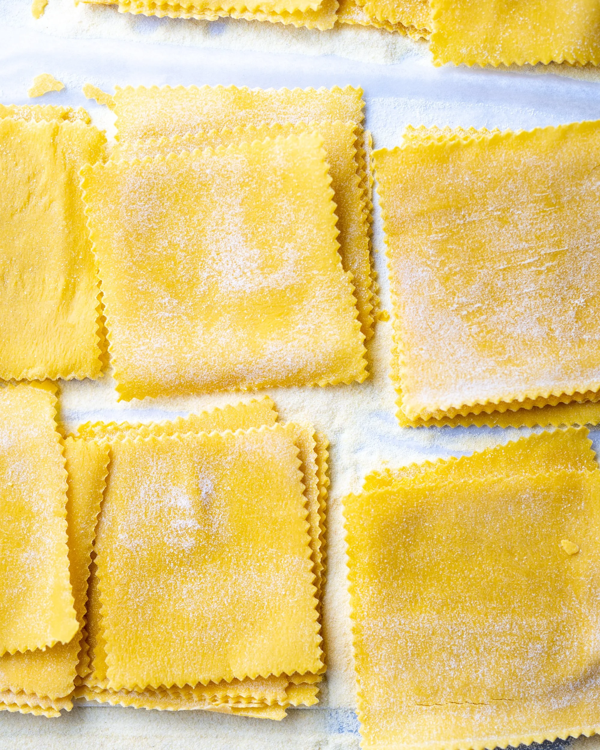 Close-up of uncooked, yellow, square-shaped lasagna pasta with wavy edges, dusted with flour.