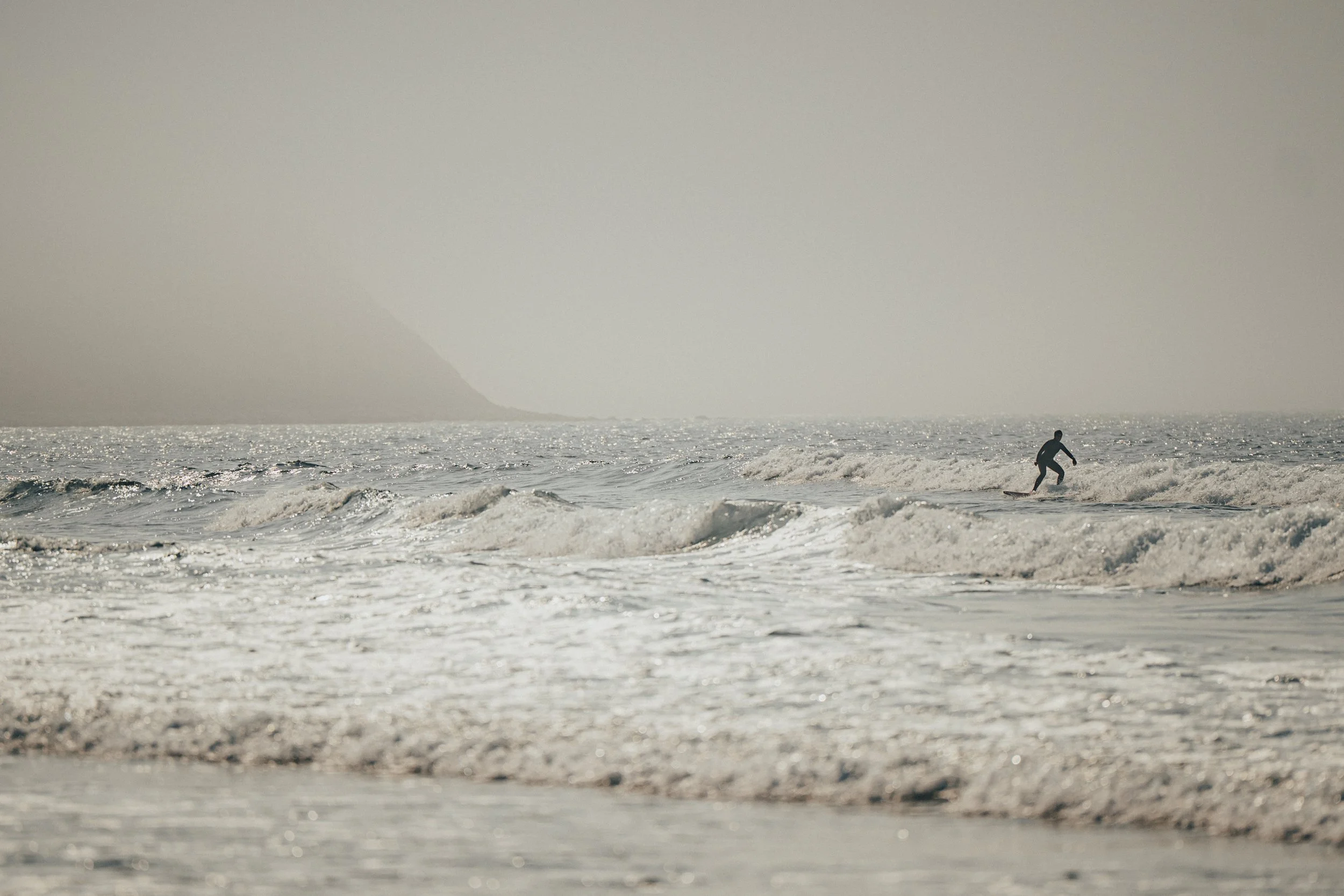 A person surfing on the ocean waves during a cloudy day with a mountainous background.
