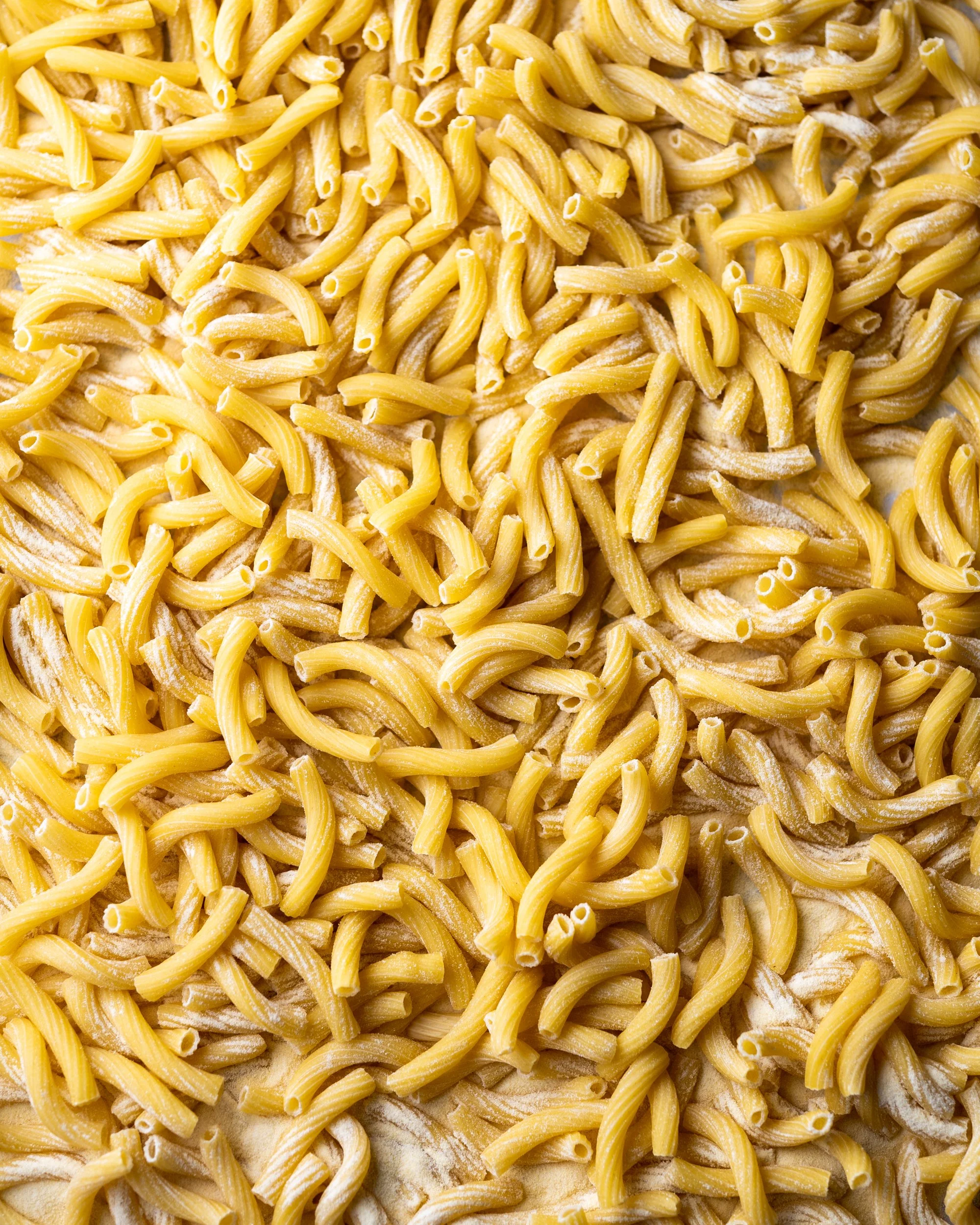 Close-up of uncooked yellow pasta noodles scattered on a floured surface.