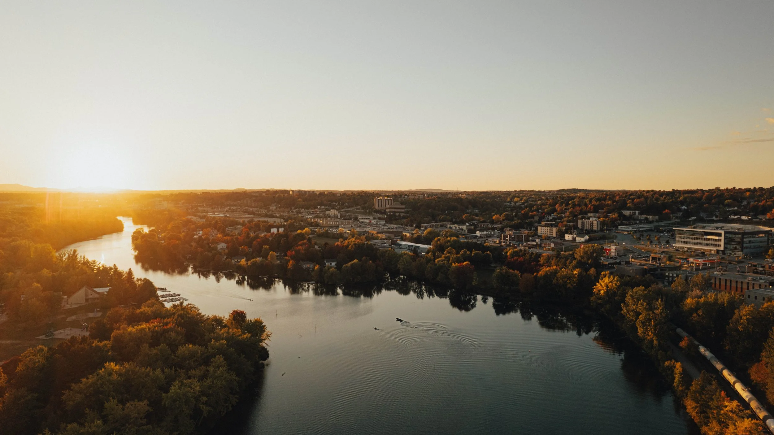 Sunset over a river cityscape with trees, buildings, and a road
