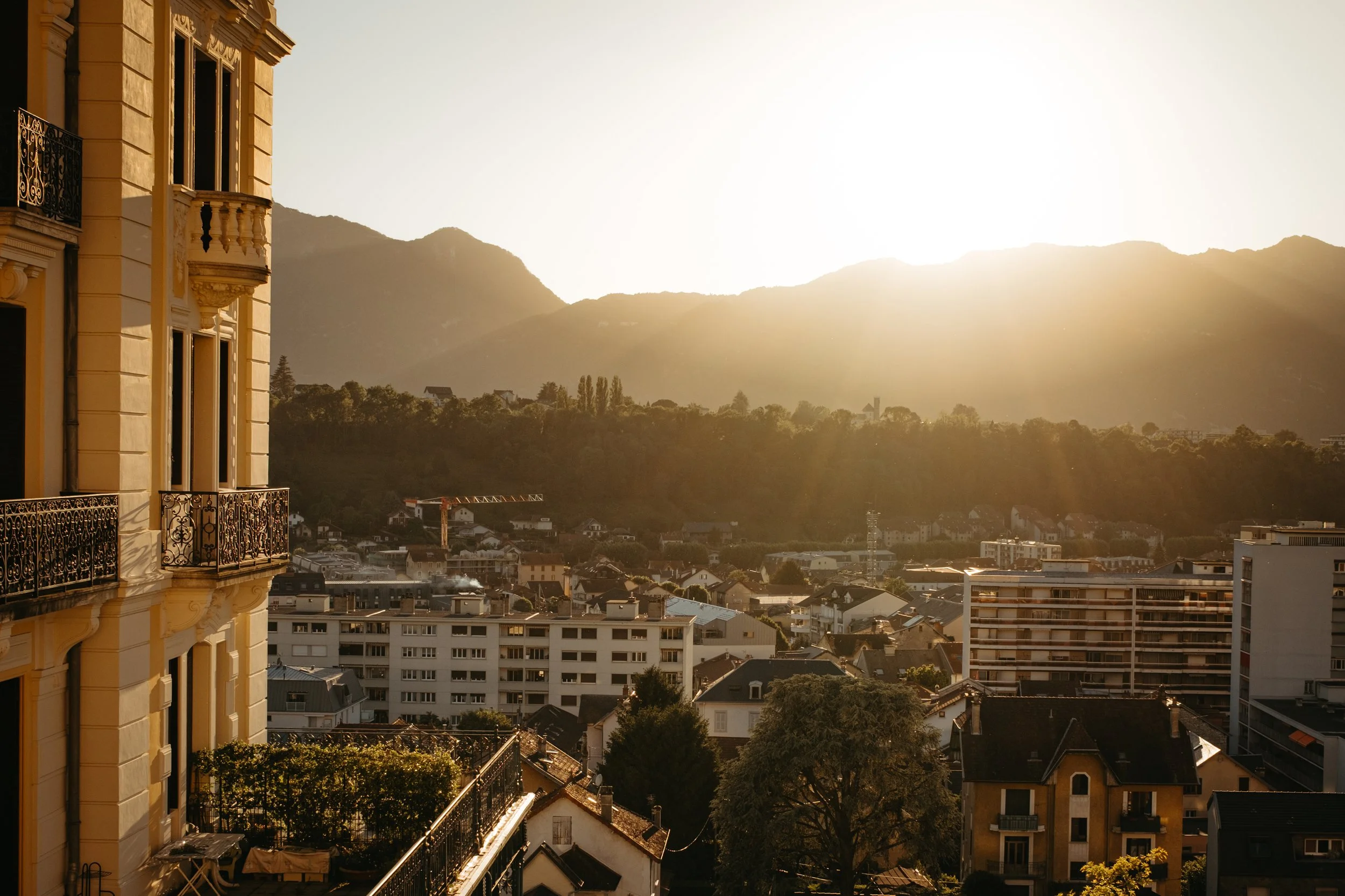 Sunset view of a city with residential buildings, a mountain range in the background, and a clear sky.