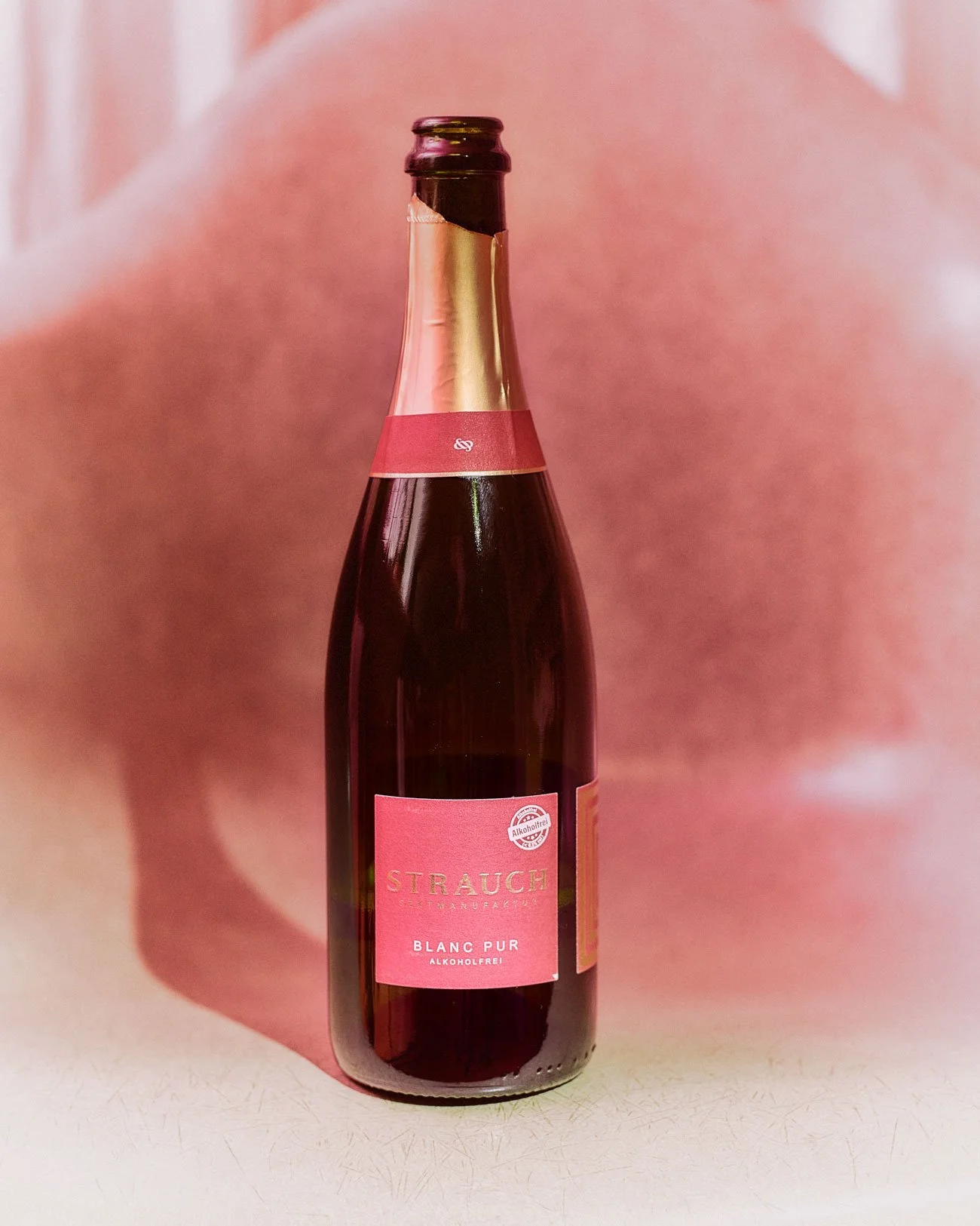 Flasche alkoholfreier Sekt mit rosa Etikett auf rosa Hintergrund.