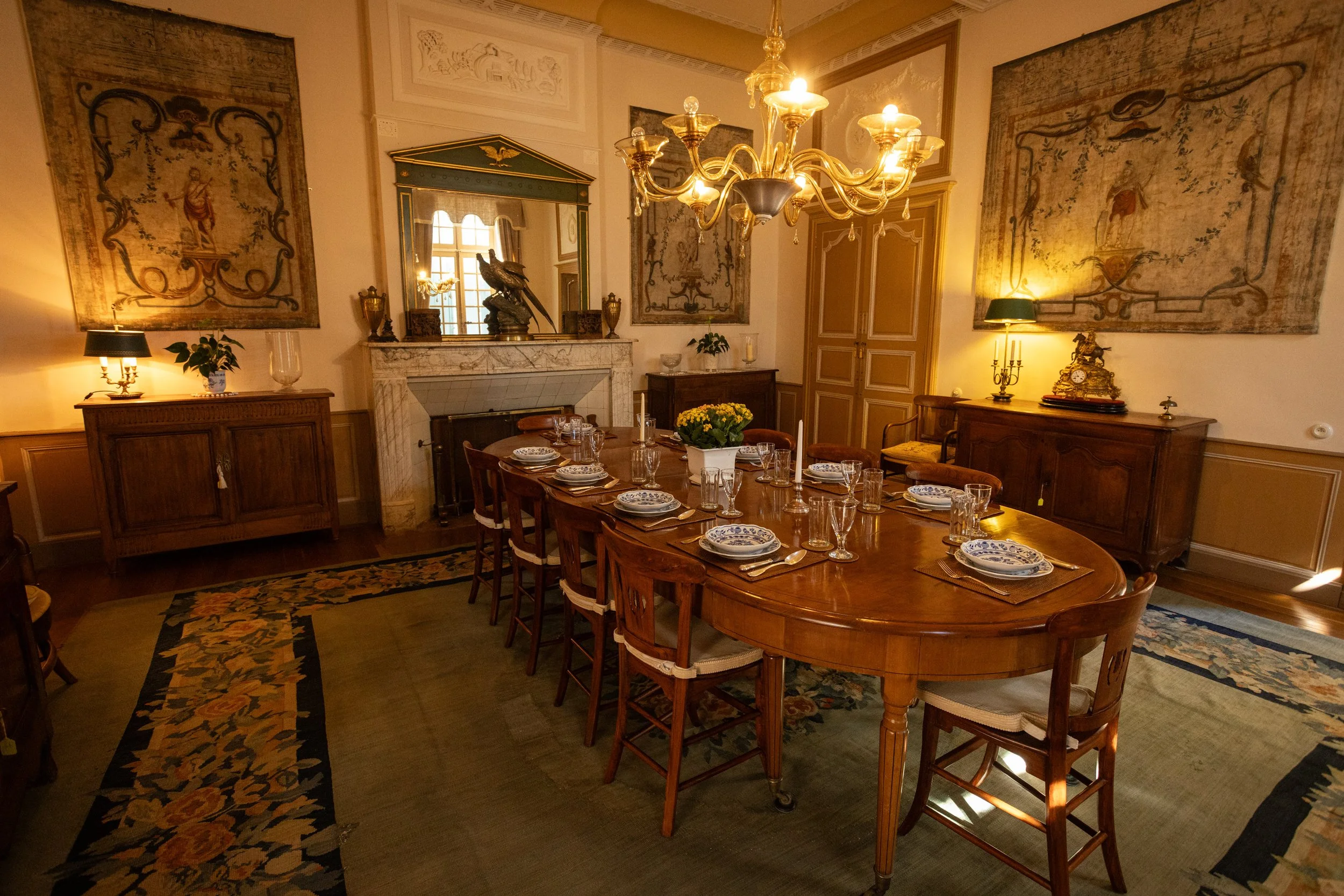 Elegant dining room at Château de Sirengard featuring period furnishings, a marble fireplace, antique artwork, and a grand table for luxury group dining.