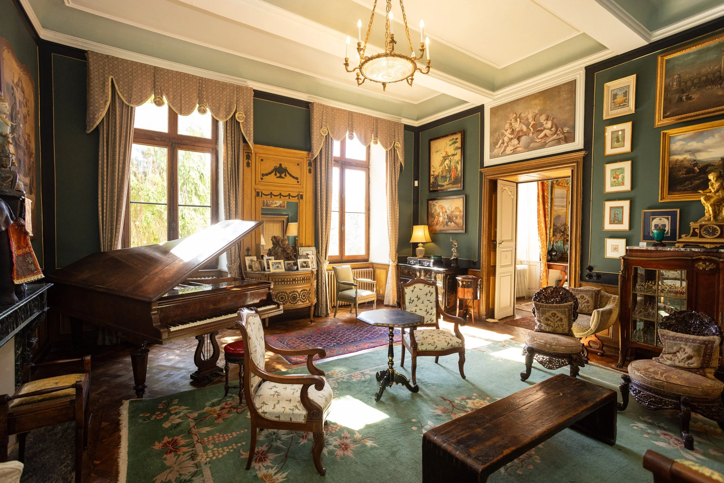 Historic salon at Château de Sirengard with a grand piano, antique furniture, high ceilings, and beautifully restored 18th-century interiors filled with natural light.