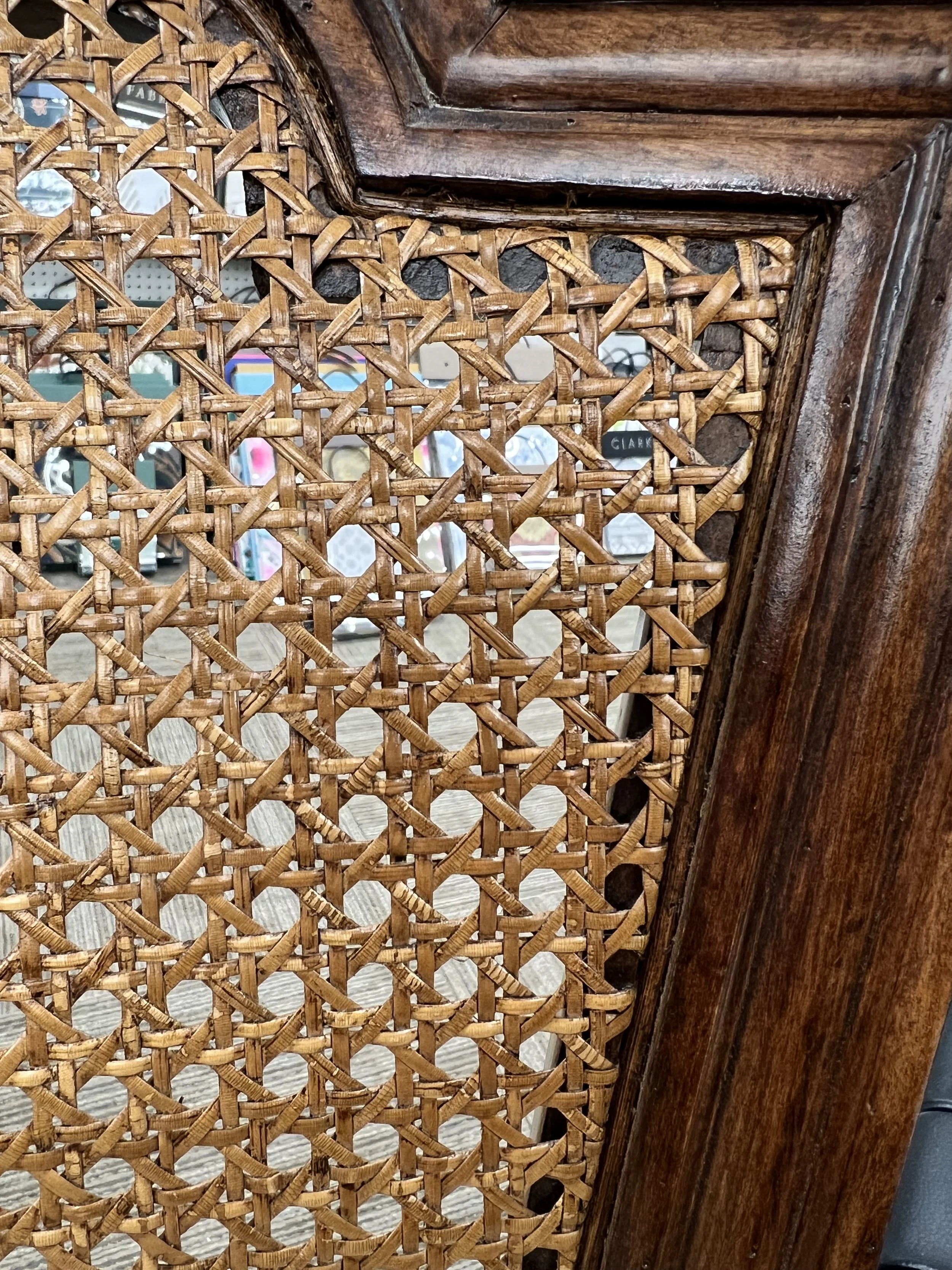 Close-up of a wooden decorative panel with a woven cane or rattan pattern, part of a furniture piece or room divider.