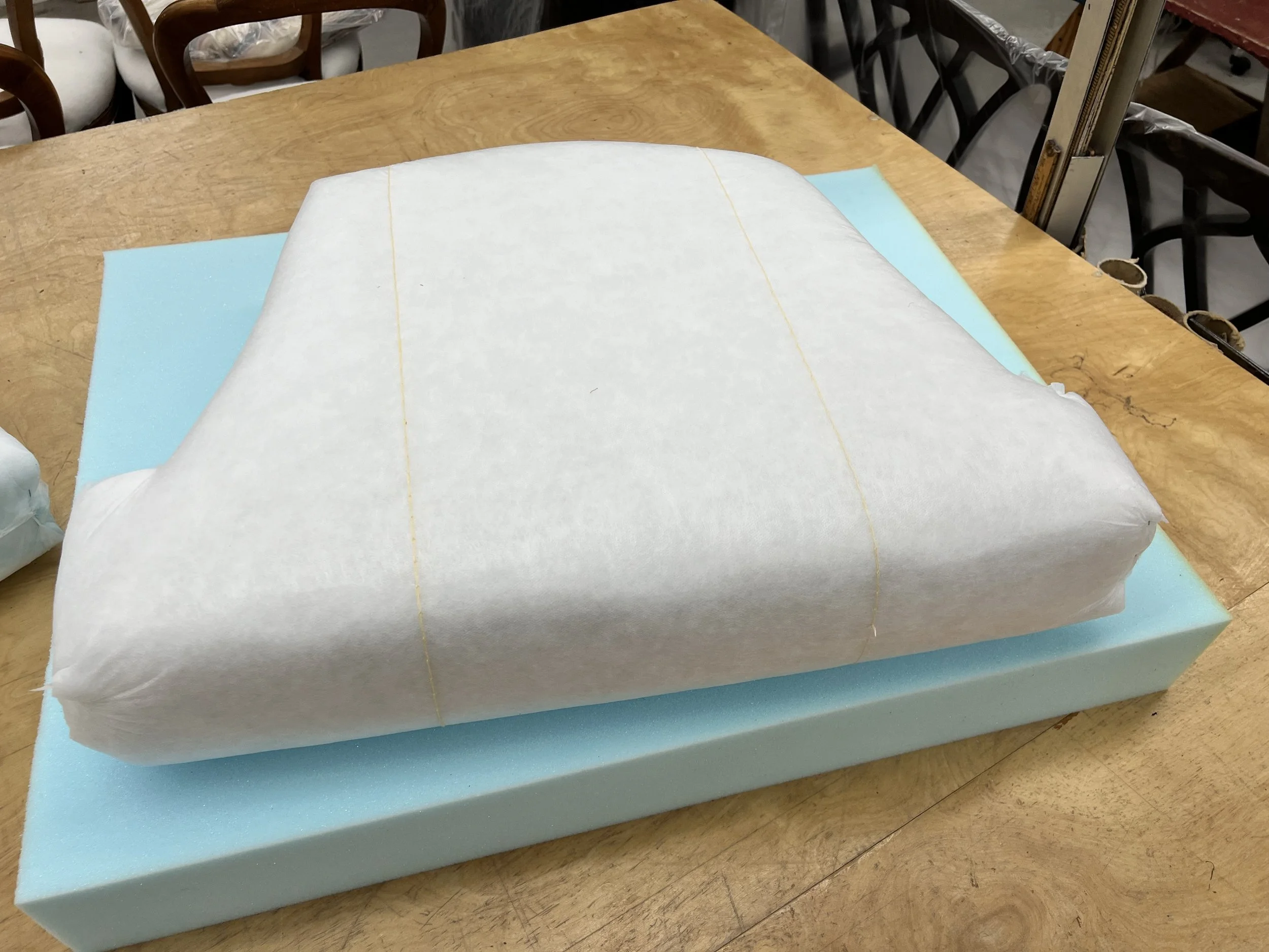 A piece of white fabric or paper placed over a light blue foam base on a wooden table, with a workshop or crafting environment in the background.