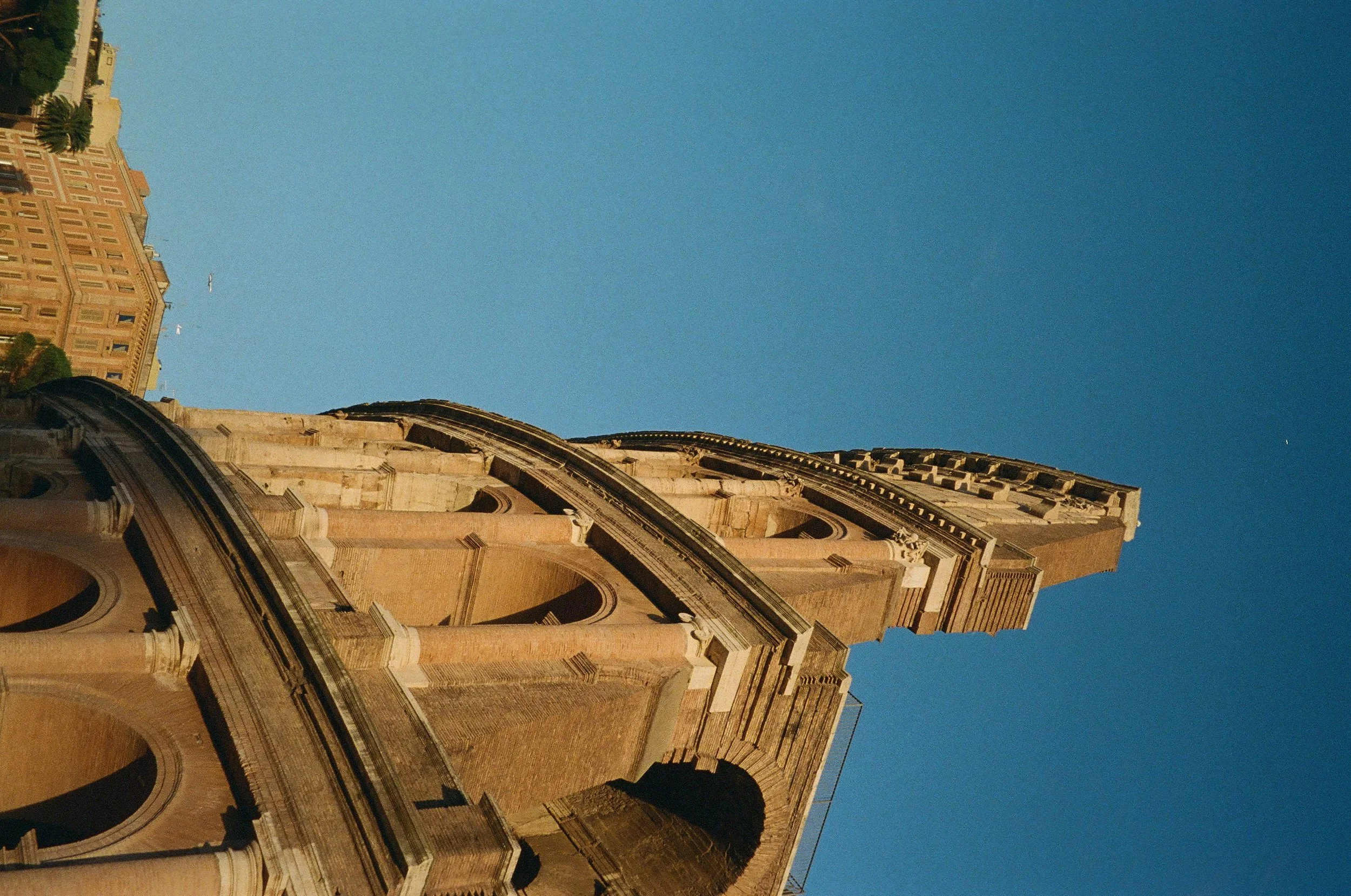 Upward view of historic church or cathedral with ornate architecture and a dome with a cross on top, against a clear blue sky.