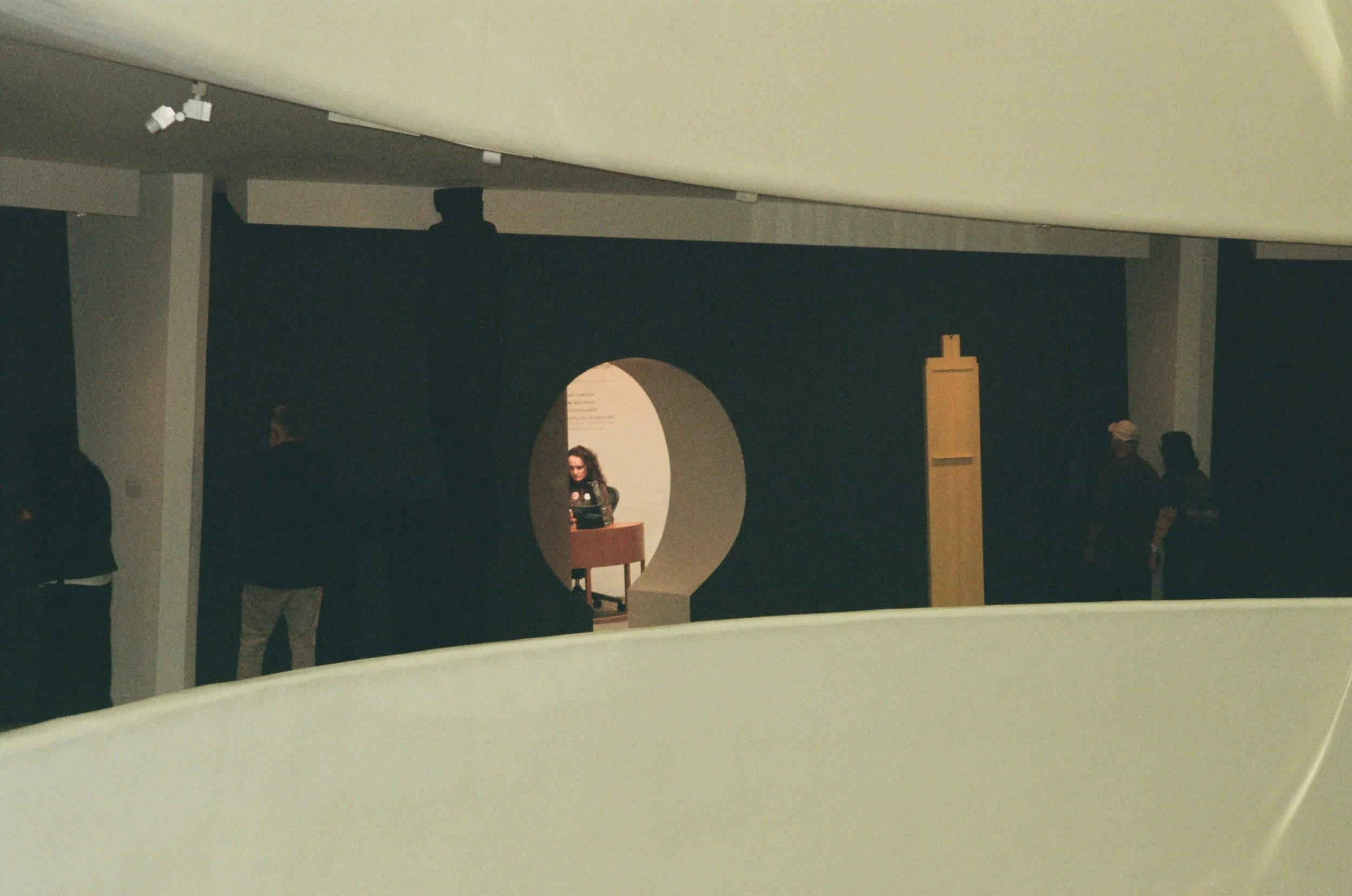People standing and conversing in a dark room with a large yellow card or sign.
