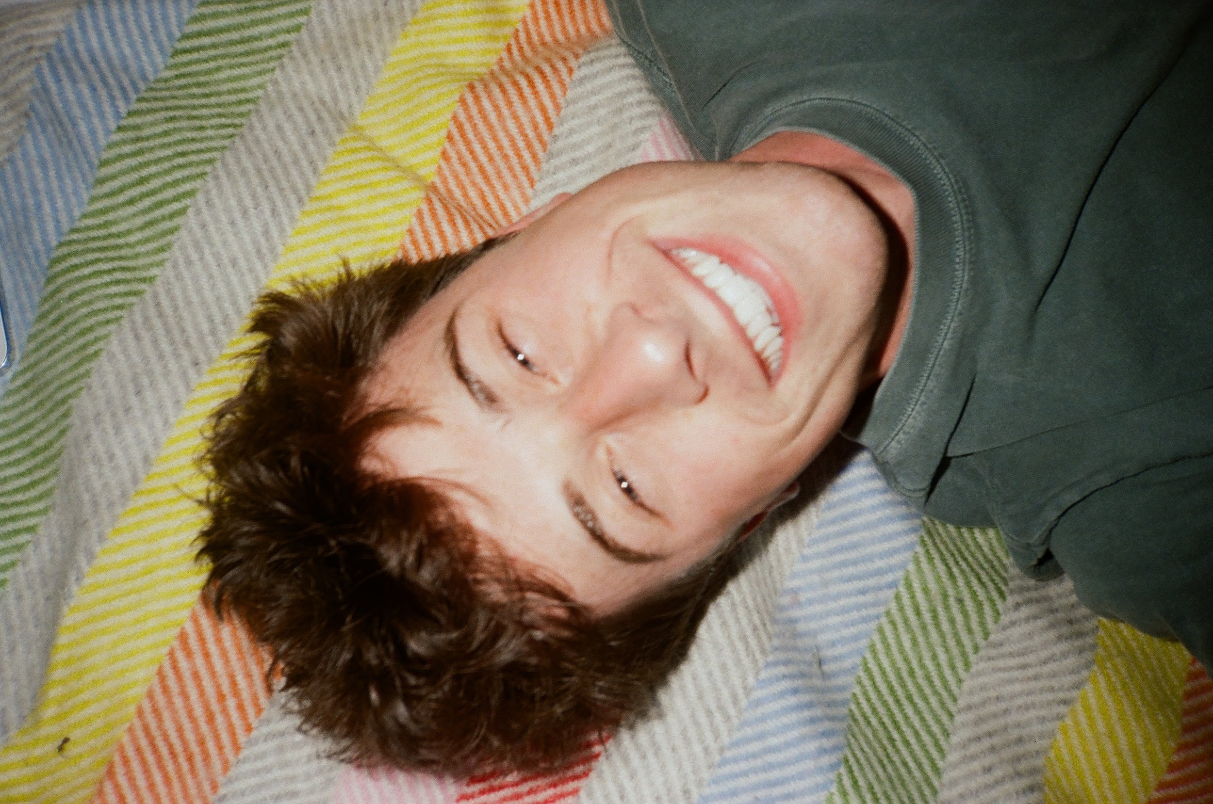 Person lying on a colorful striped quilt, smiling with eyes closed.