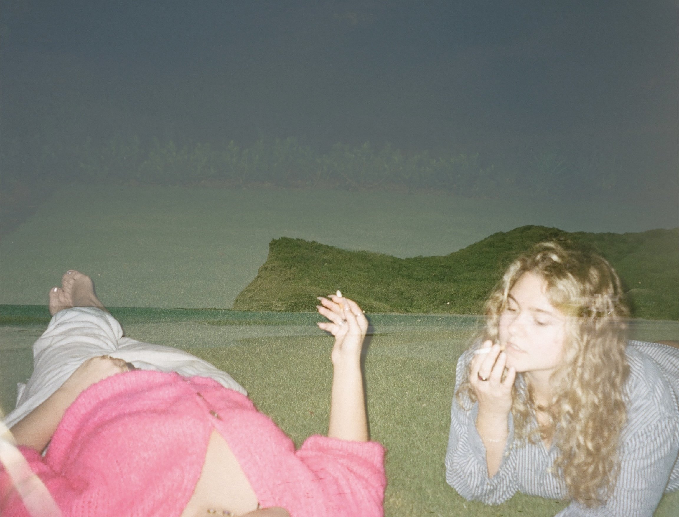 People lying on grass, smiling and laughing, with mountainous landscape in the background.