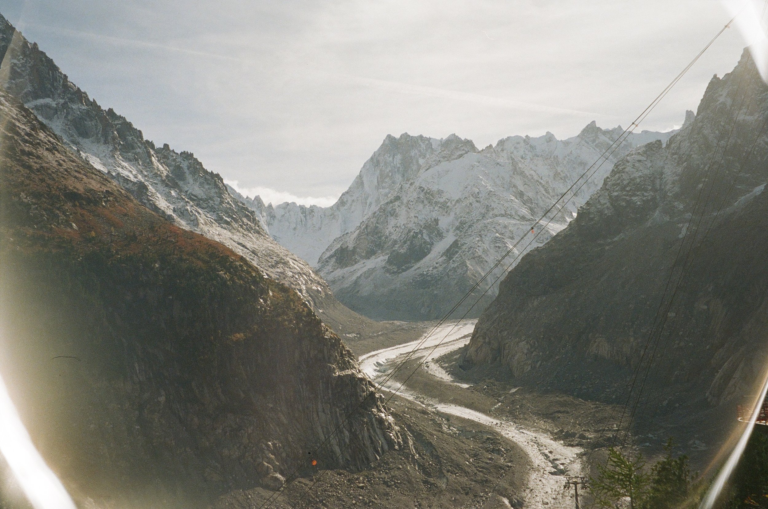 Snow-capped mountain peaks and rugged terrain seen through a window or viewfinder with power lines crossing the scene.
