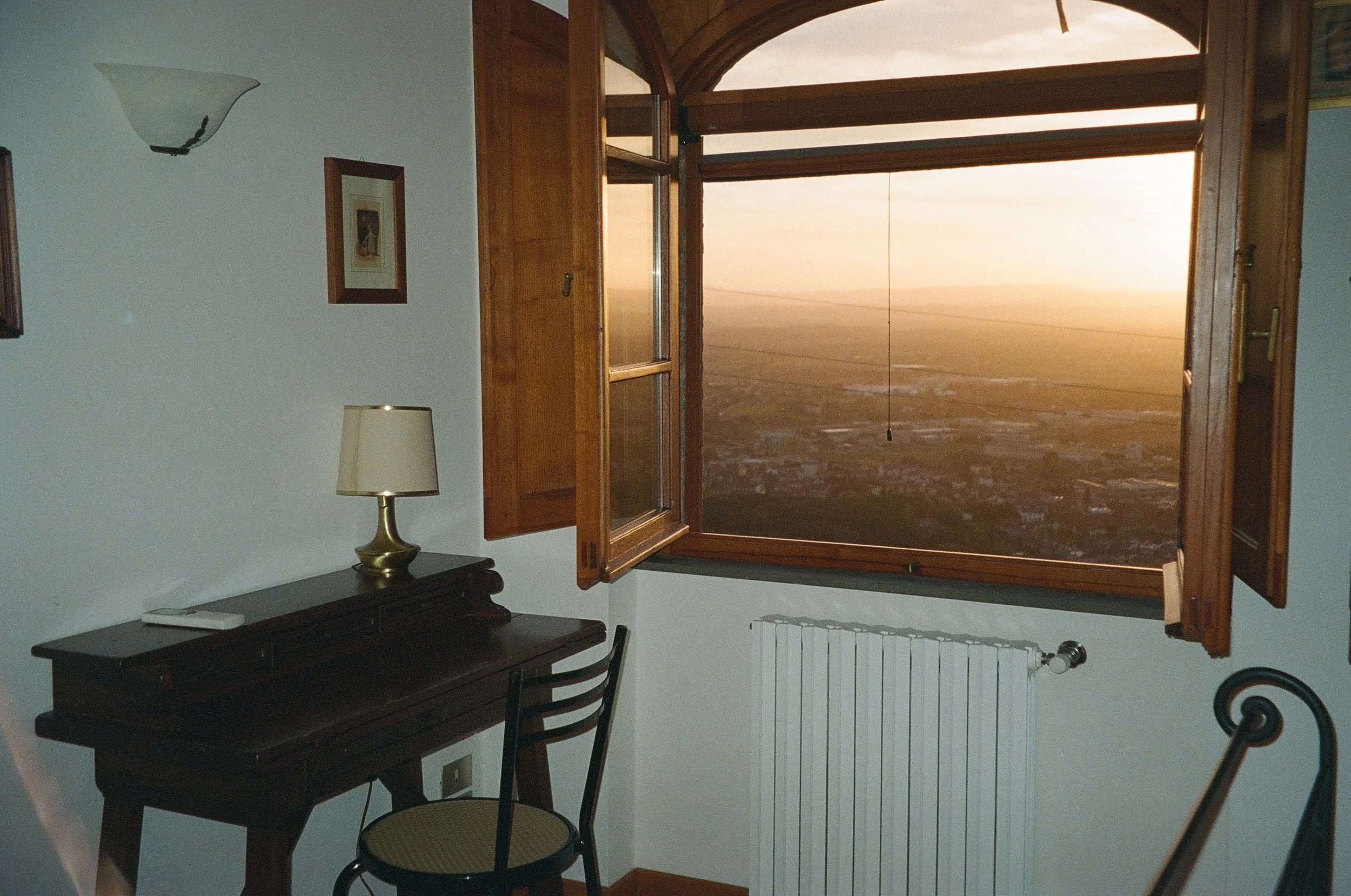 A windowsill open to a view of a desert landscape with hills in the distance at sunset.