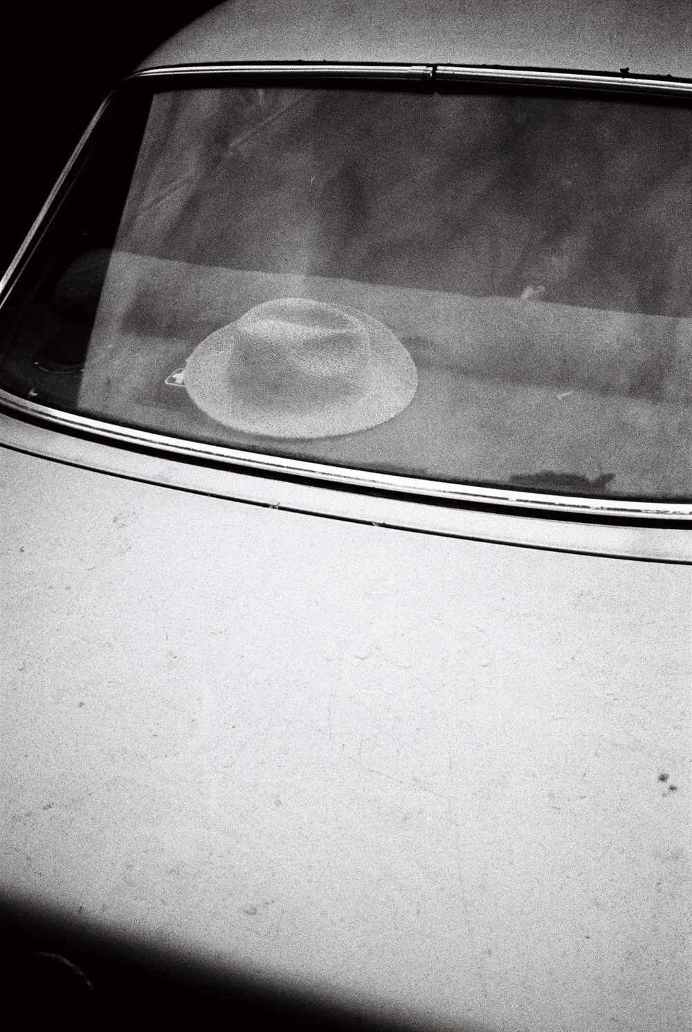 A hat on the dashboard of a vintage car viewed through the windshield.