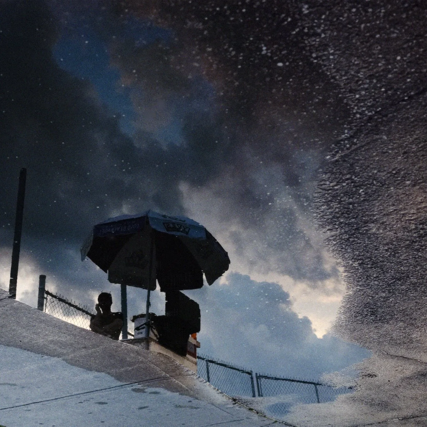 Reflection of a food stand with an umbrella on a puddle at dusk