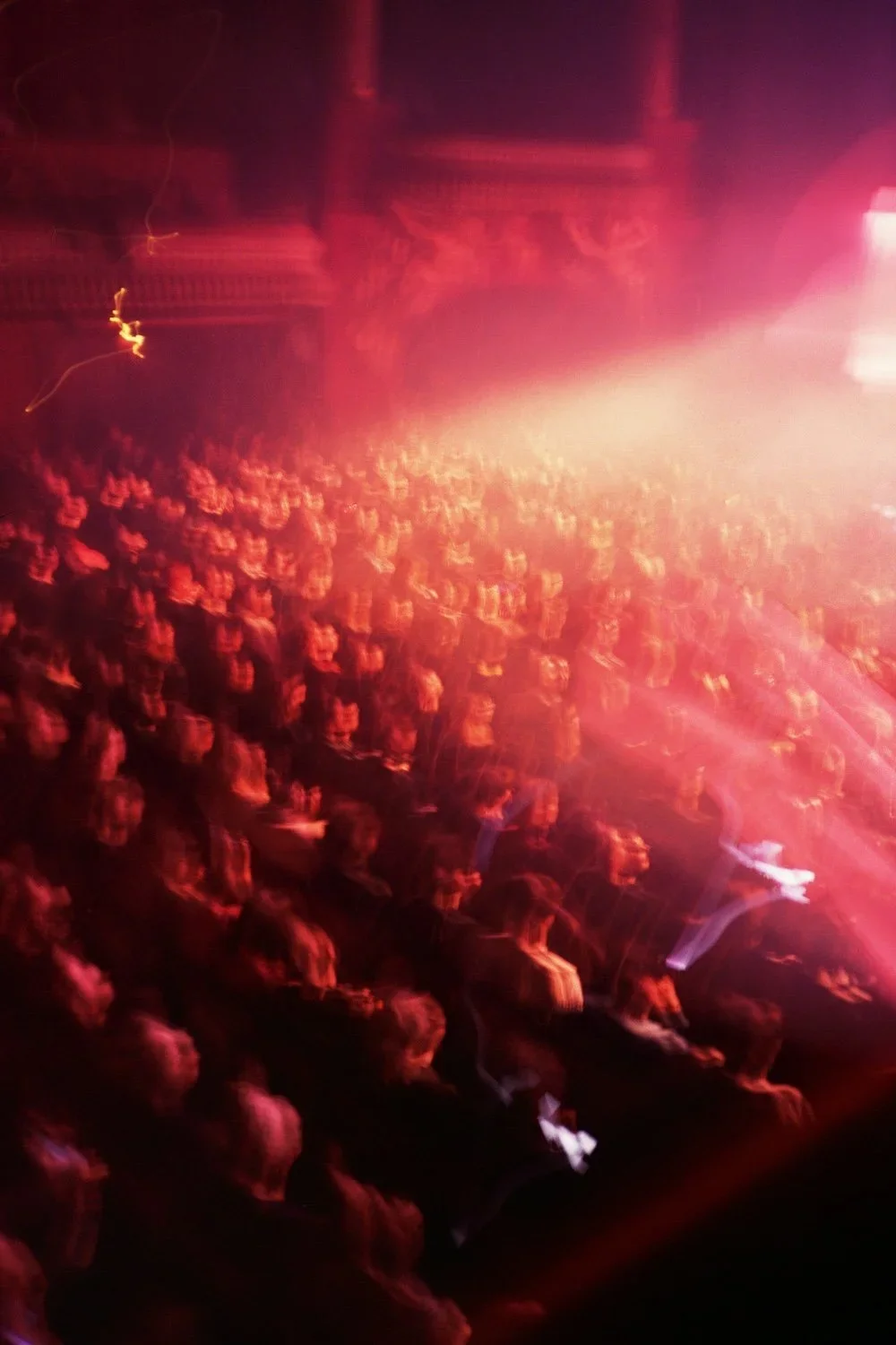 Crowd of people attending a concert or event in a dimly lit venue with red and purple lighting.