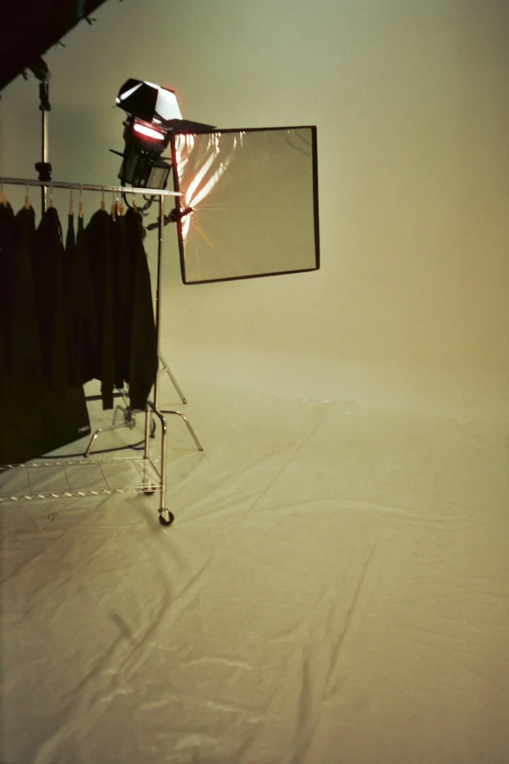 A mirror with a crack, a clothing rack with black garments, and a spotlight in a photography or video studio.