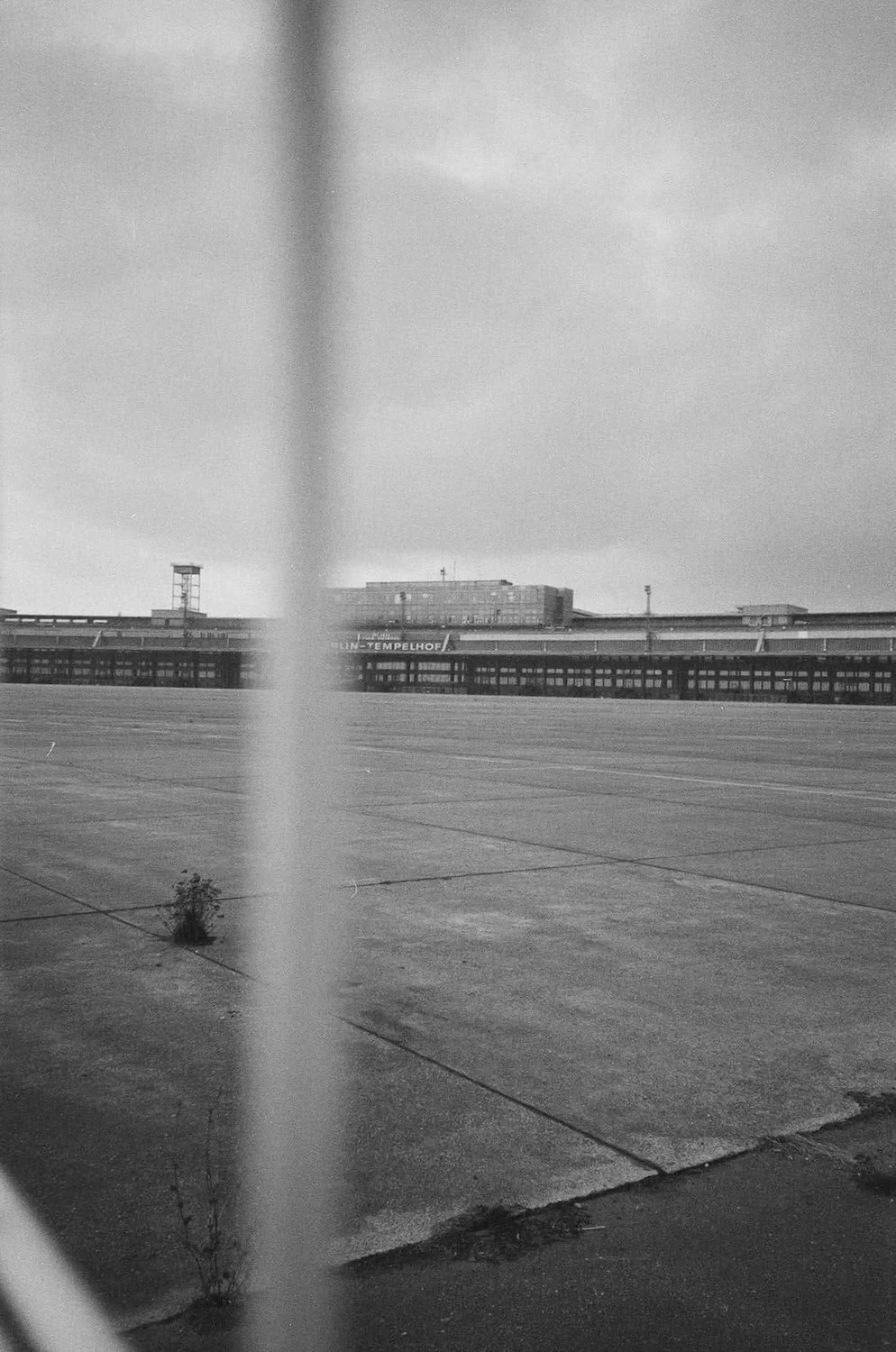 Black and white photo of an airport runway with a distant building in the background, partially obscured by a vertical object in the foreground.