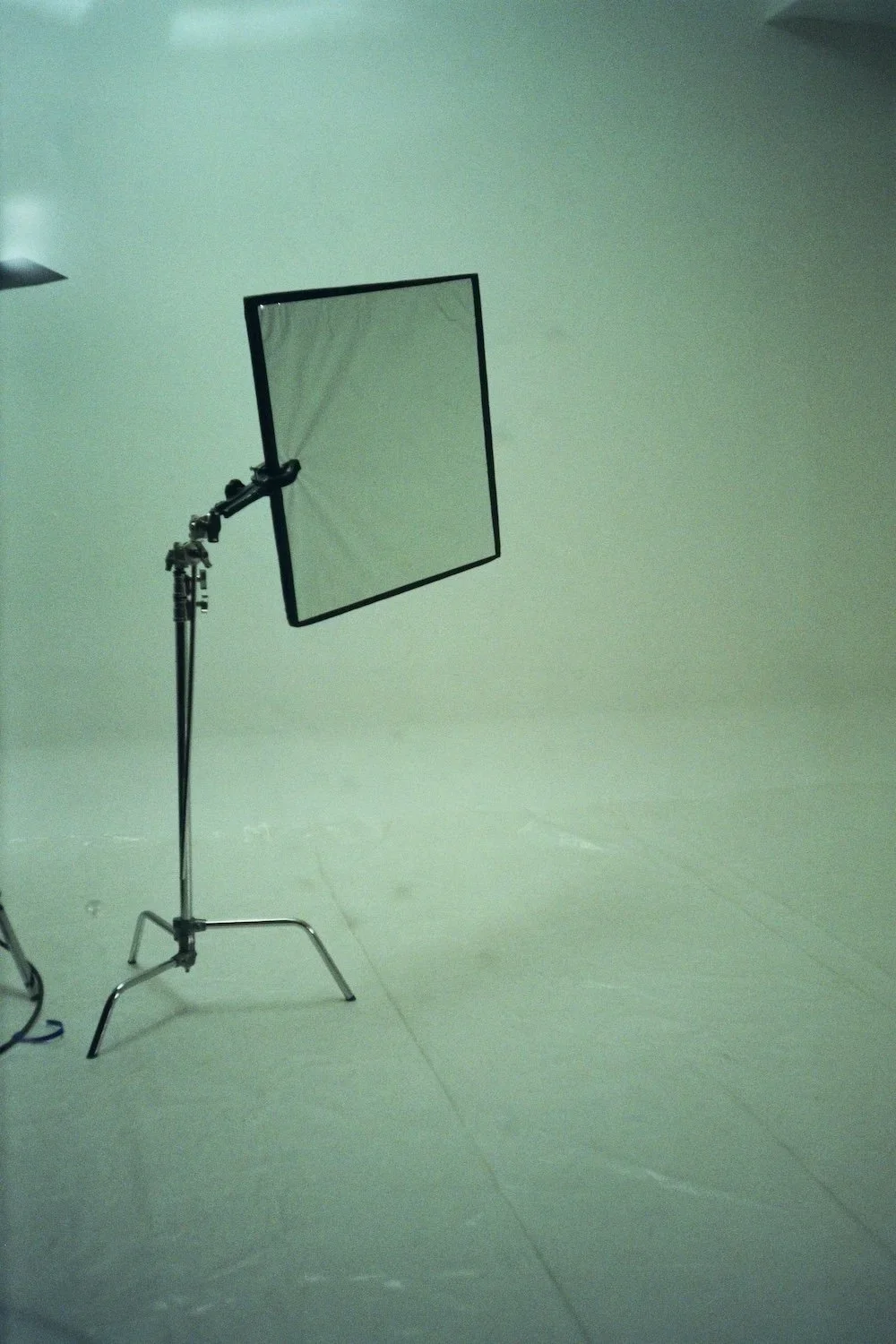 Photography studio with a studio light stand and a black square reflector on a plain white backdrop.