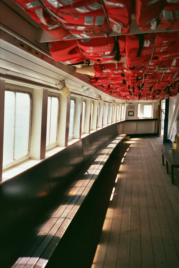 Empty window-lined deck with sunlight creating striped shadow patterns on wooden floor and black seating.