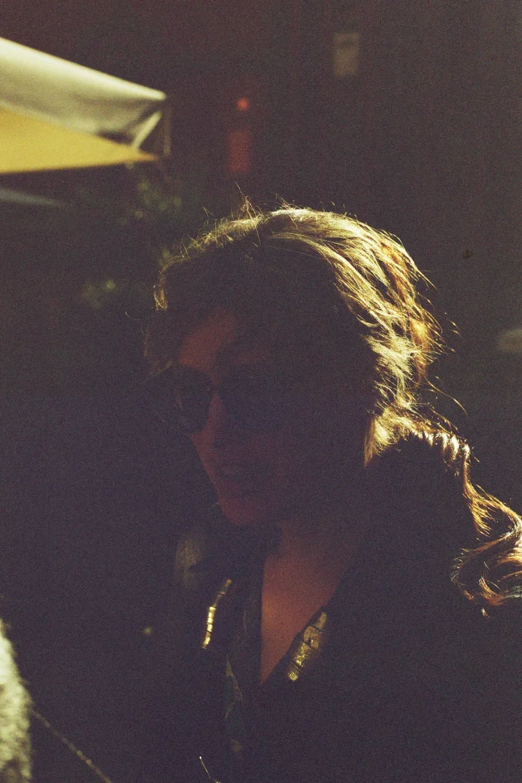 A woman with wavy hair and sunglasses outdoors in sunlight.