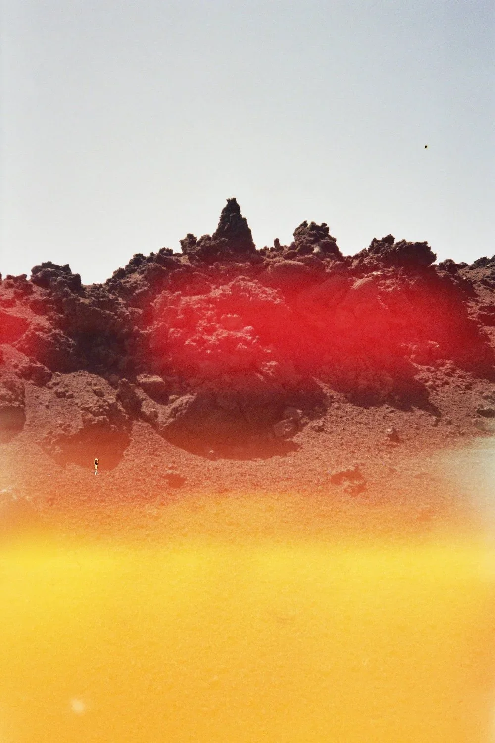 A rocky landscape with a large mound of dark volcanic rock under a bright sky, with a red lens flare and a yellowish obstruction at the bottom of the image.