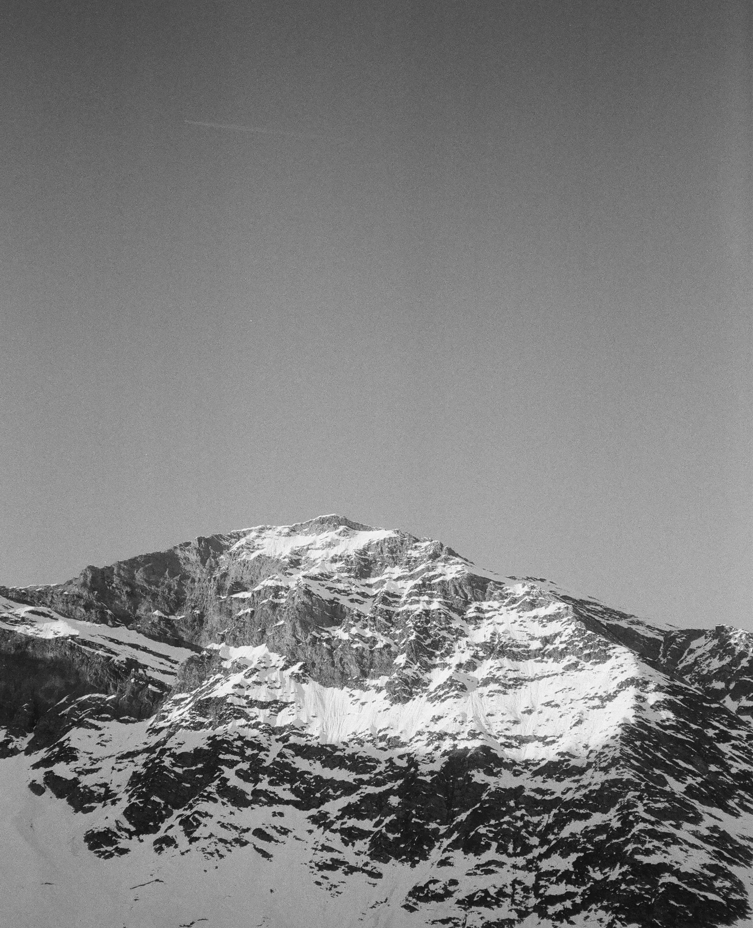 Black and white photograph of a snow-capped mountain peak with a clear sky in the background.